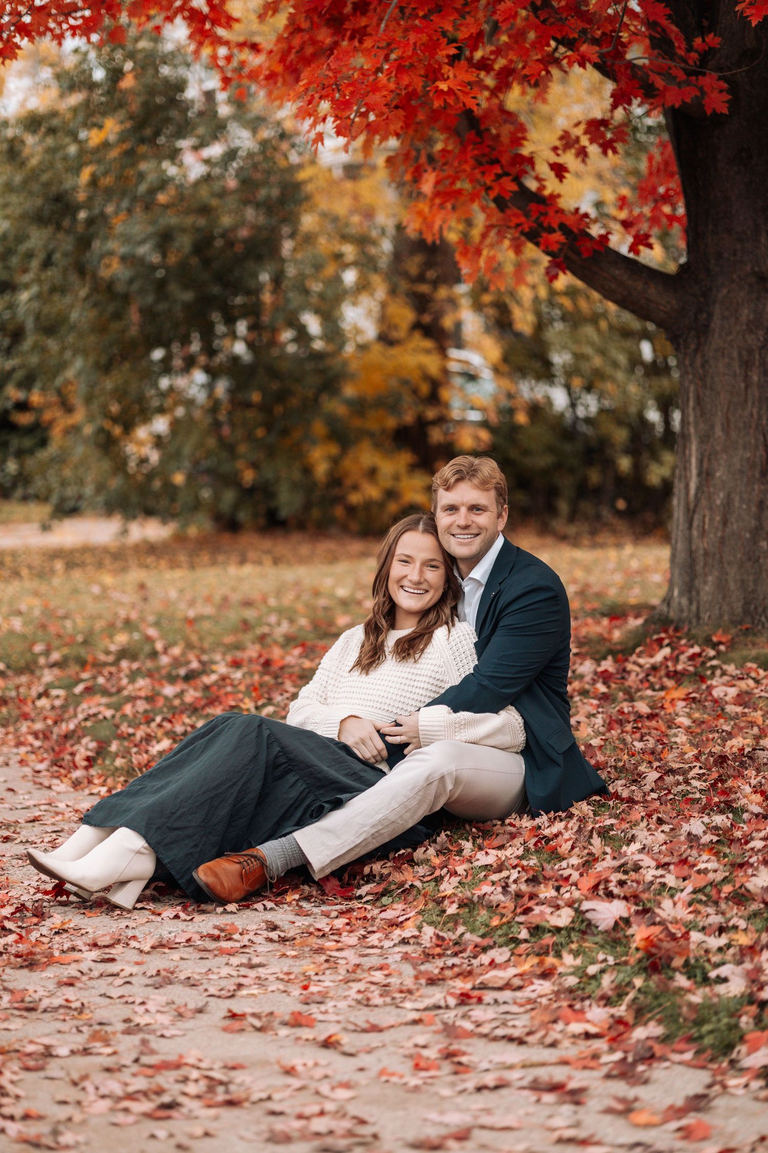 Couple lying in vibrant red autumn leaves during photoshoot.