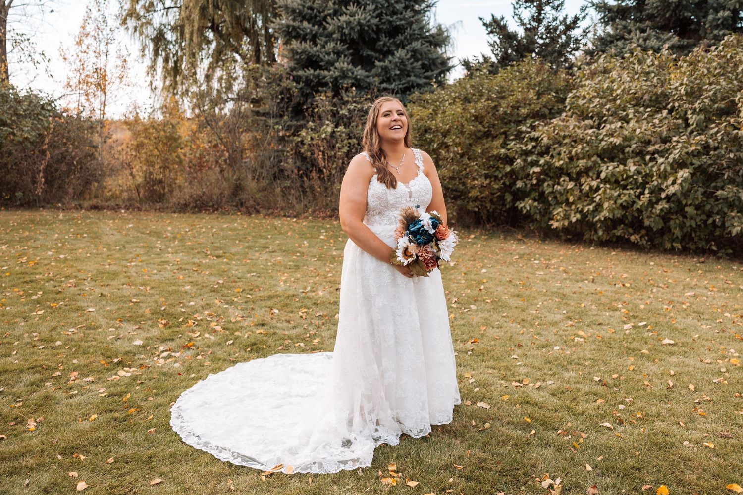 White lace wedding dress train spreads across grass during fall outdoor photography session.