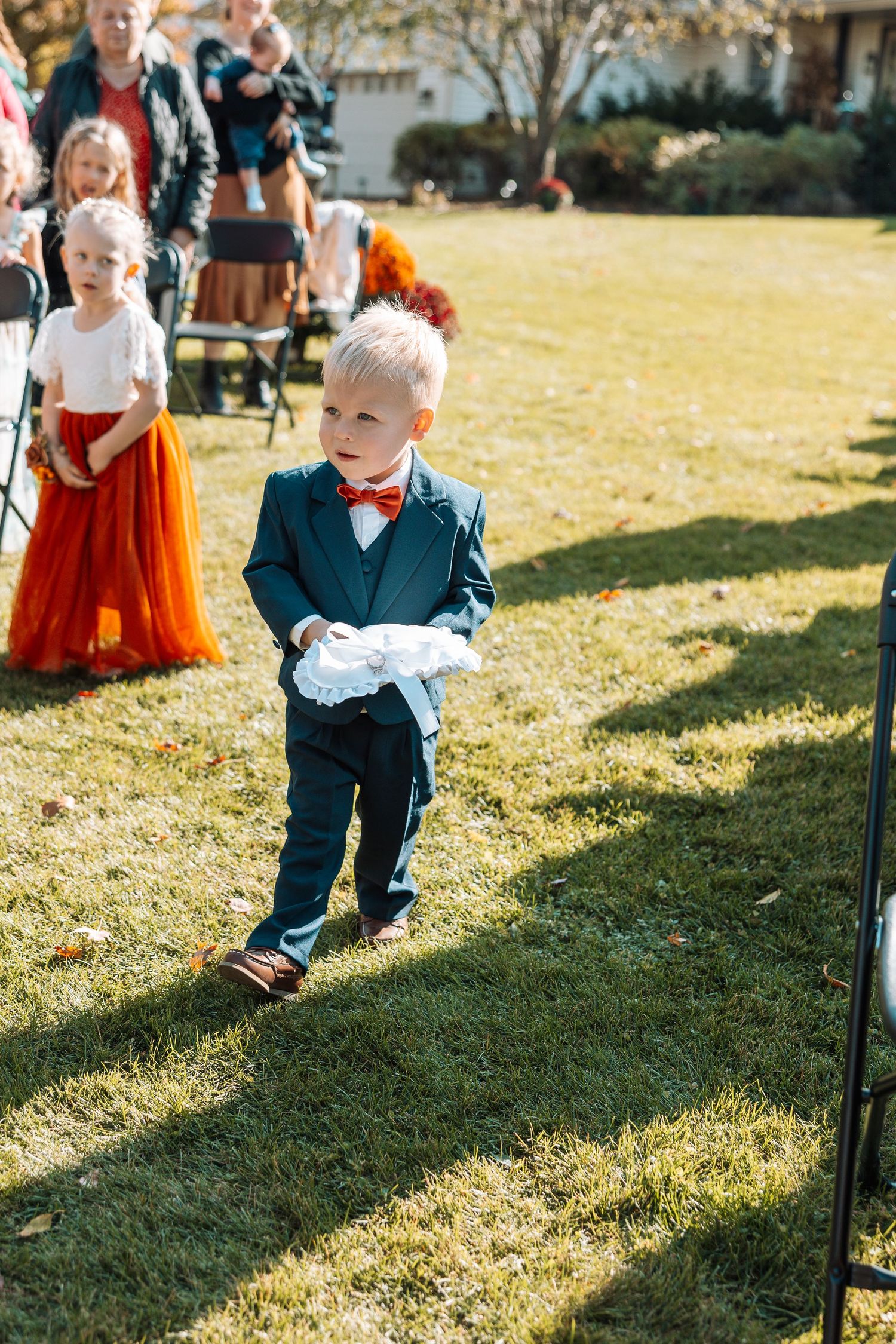 Ring bearer in navy suit and bow tie walking on grass during outdoor ceremony.