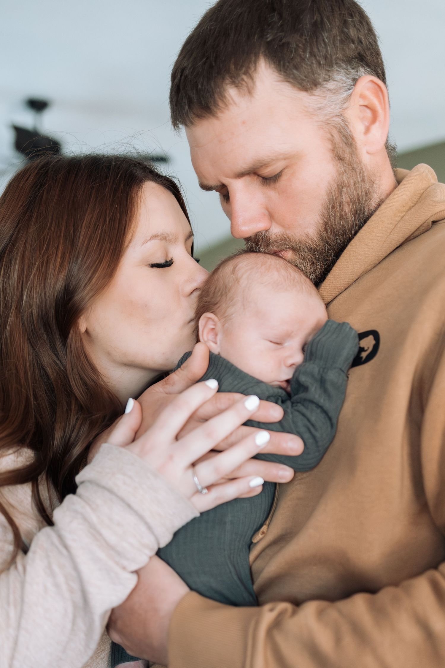 Intimate family moment showing parents sharing tender kisses with their baby in casual attire.