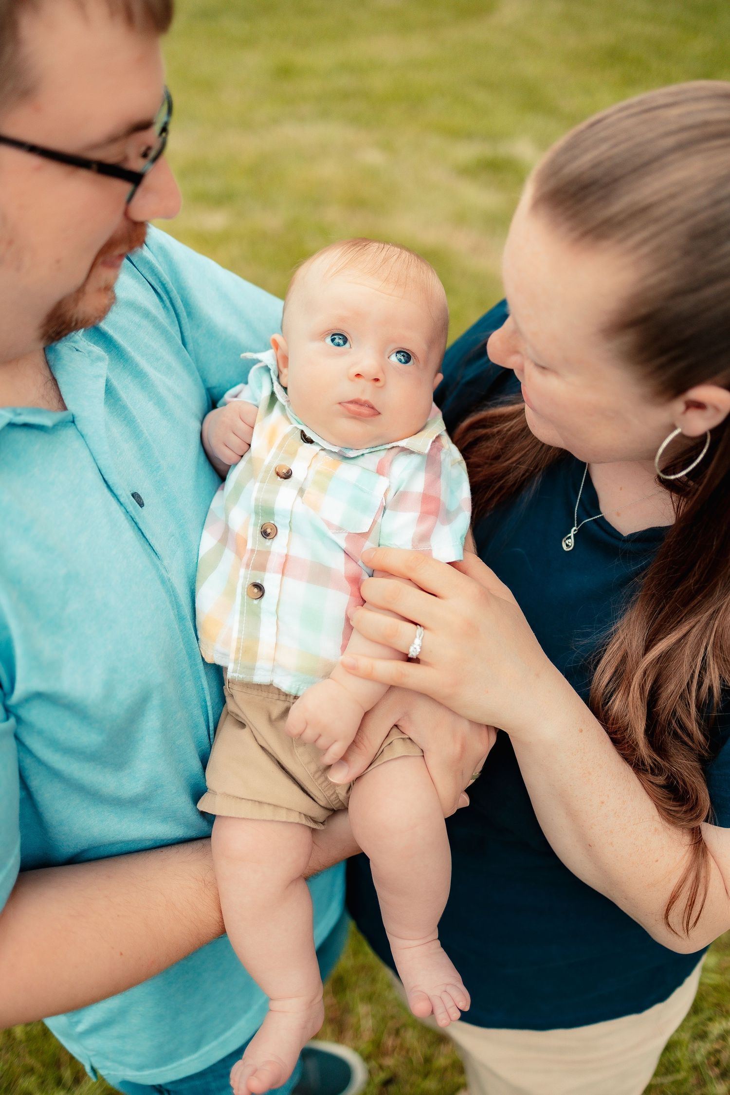 Parents in coordinating blue and navy outfits hold their infant during an outdoor photo session.