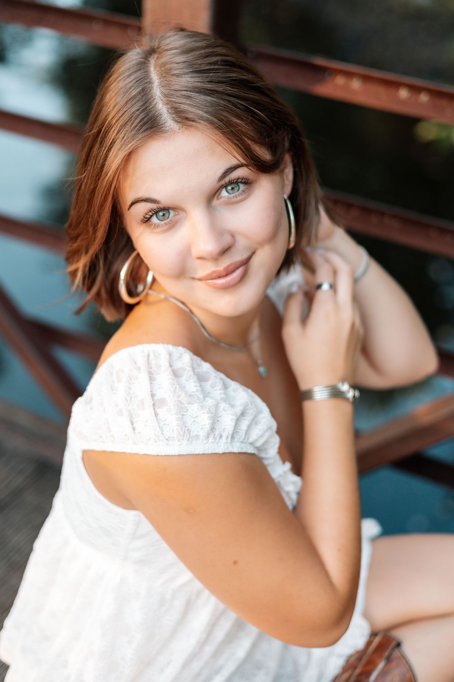 Person in white dress posing on wooden bench during outdoor portrait session.