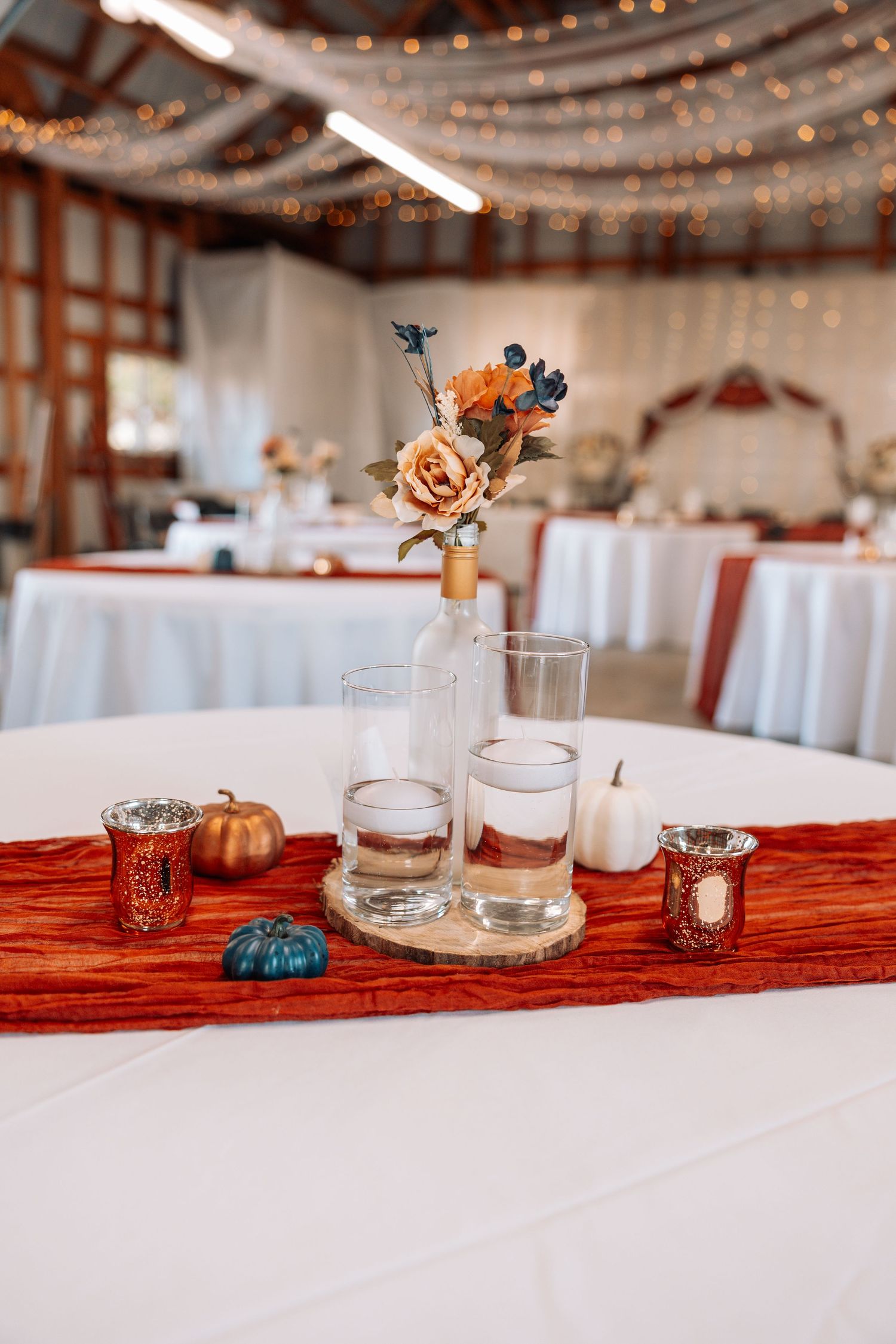 Wedding reception table with rustic decor, string lights, and orange floral centerpieces.