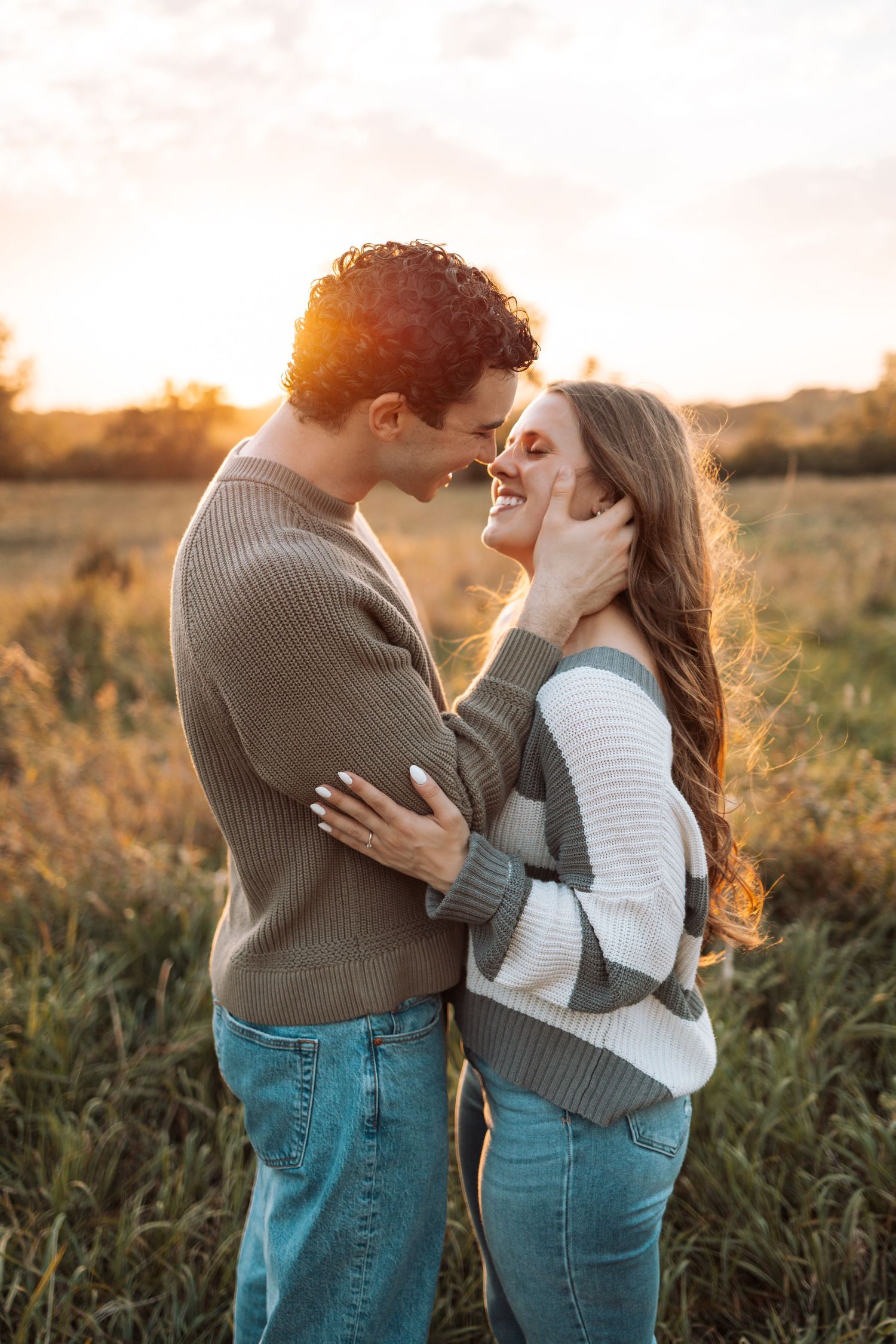 Couple embracing in a field during golden hour wearing matching sweaters and jeans.
