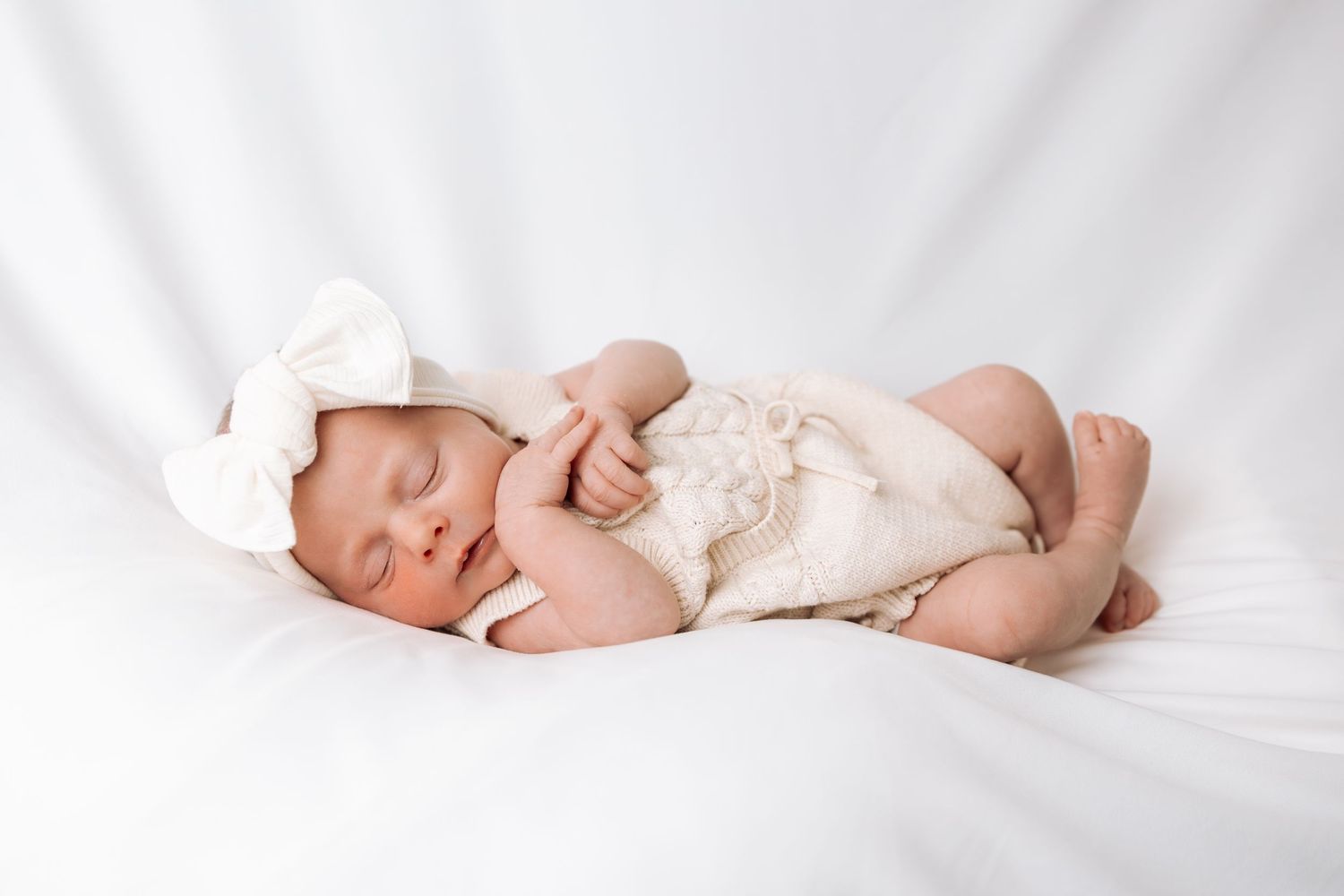 Minimalist newborn photography on white backdrop capturing peaceful sleeping pose.