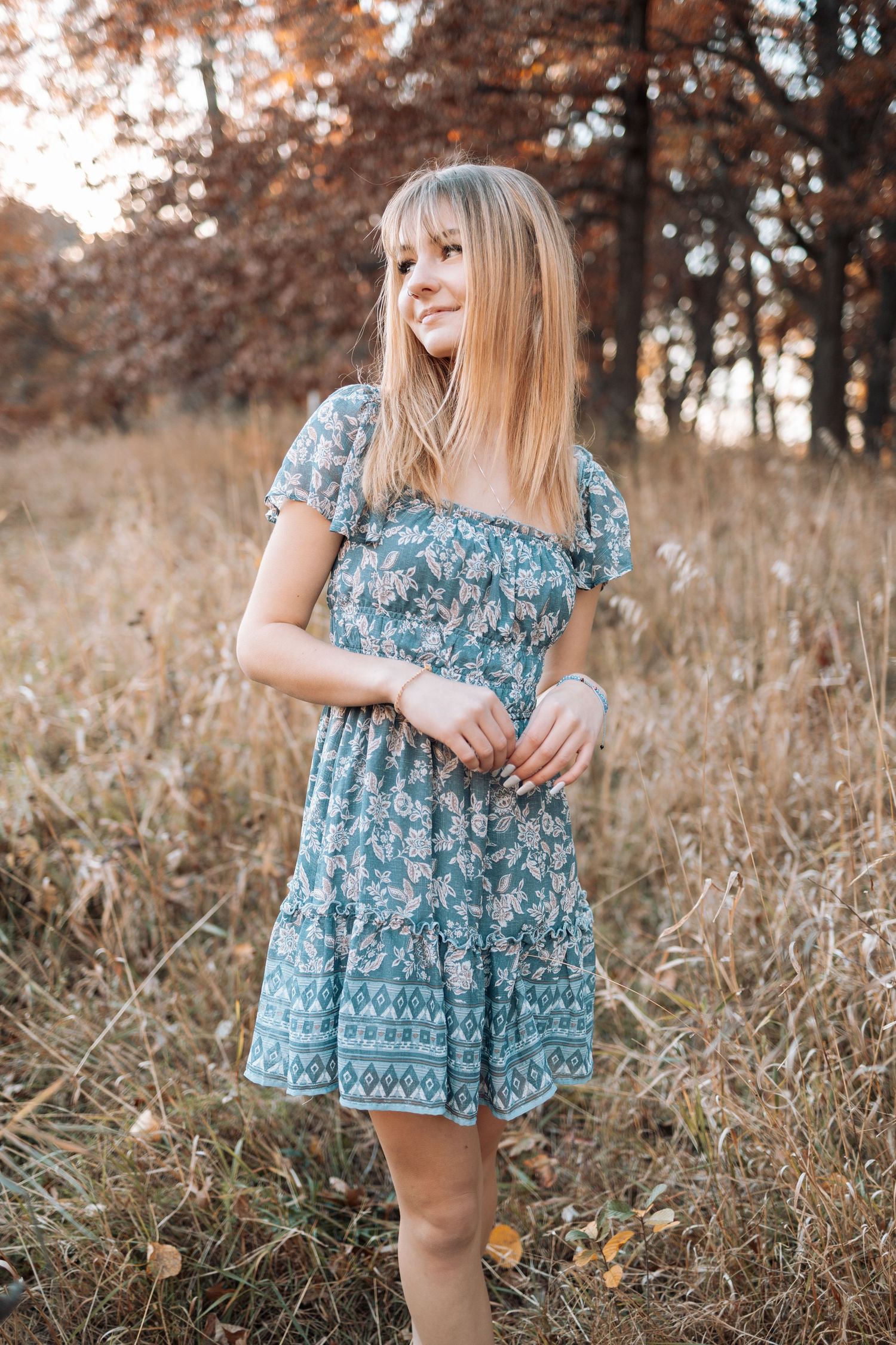 Woman in floral blue dress poses in autumn field at sunset with Kenzie Ayla Images in the Twin Cities MN area.