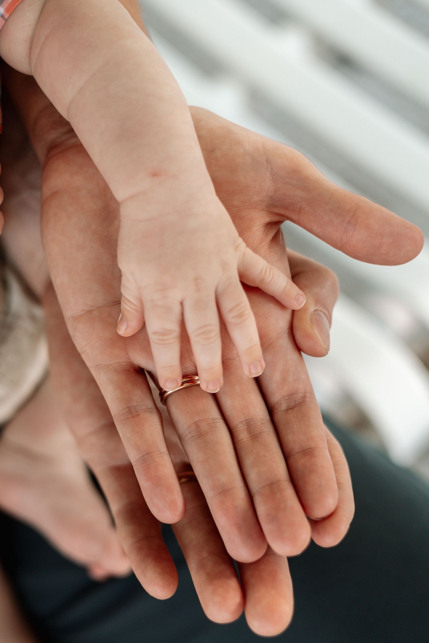 Close-up of hands with wedding rings intertwined against light background.