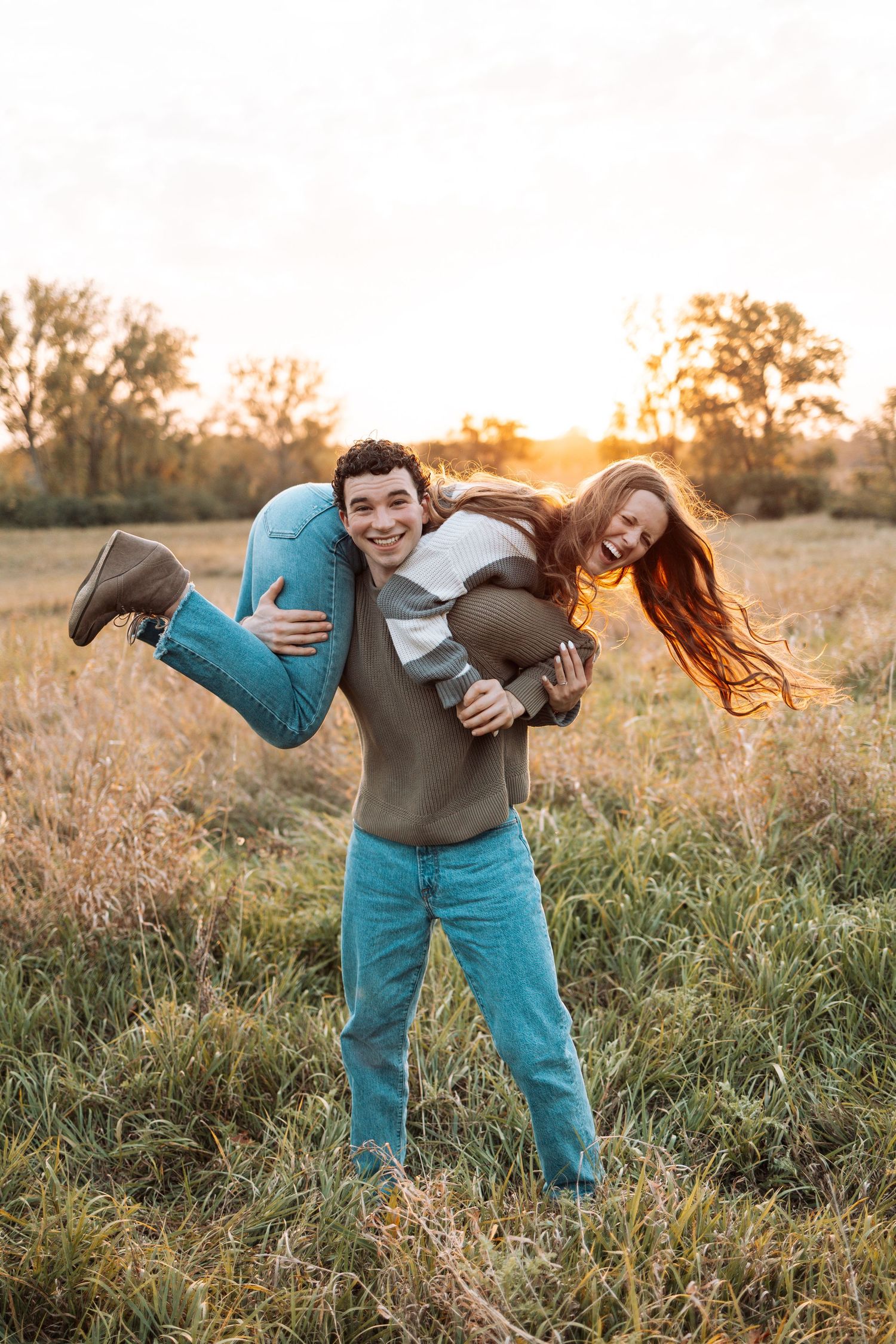 Playful couple having fun with lifting poses in a sunlit meadow.
