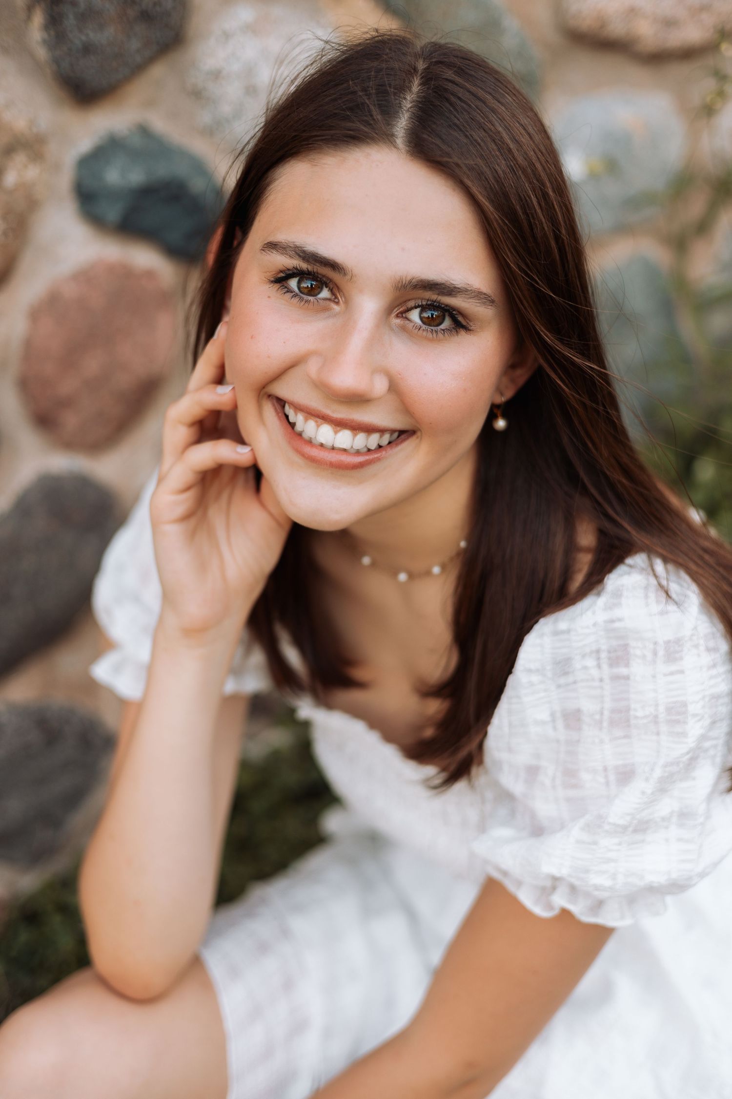 Portrait of a person in a white dress smiling against a stone wall background.
