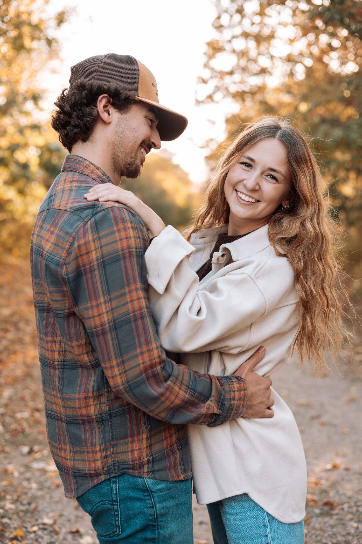 Couple sharing joyful moments in autumn wearing plaid and cream colored outfits.