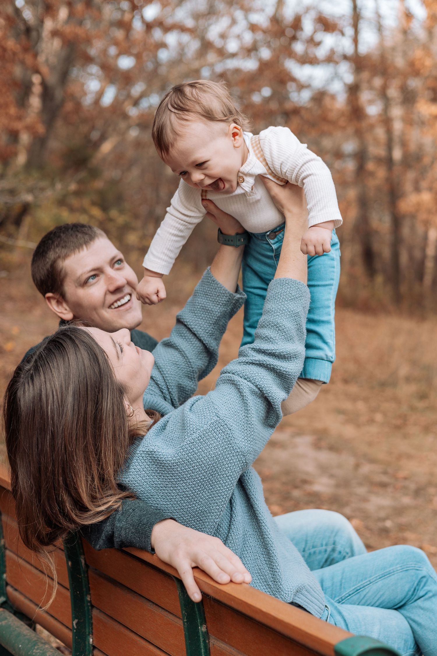 Joyful family plays together on wooden bench in autumn forest setting.