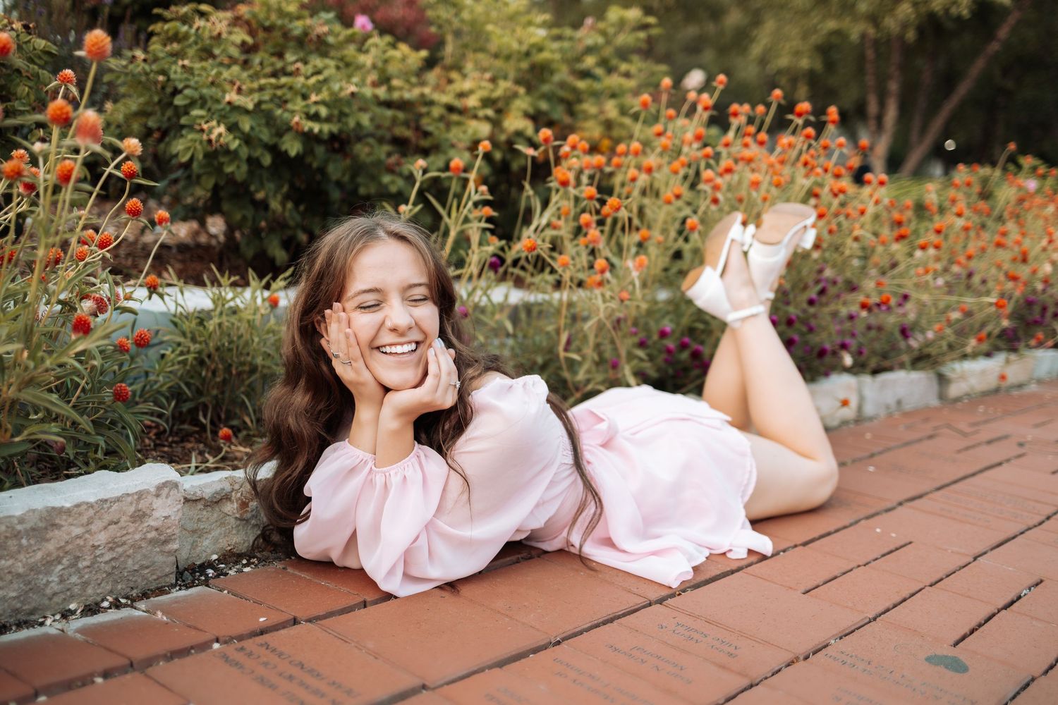 Candid garden photoshoot featuring someone in pink lounging near orange and red flowers.