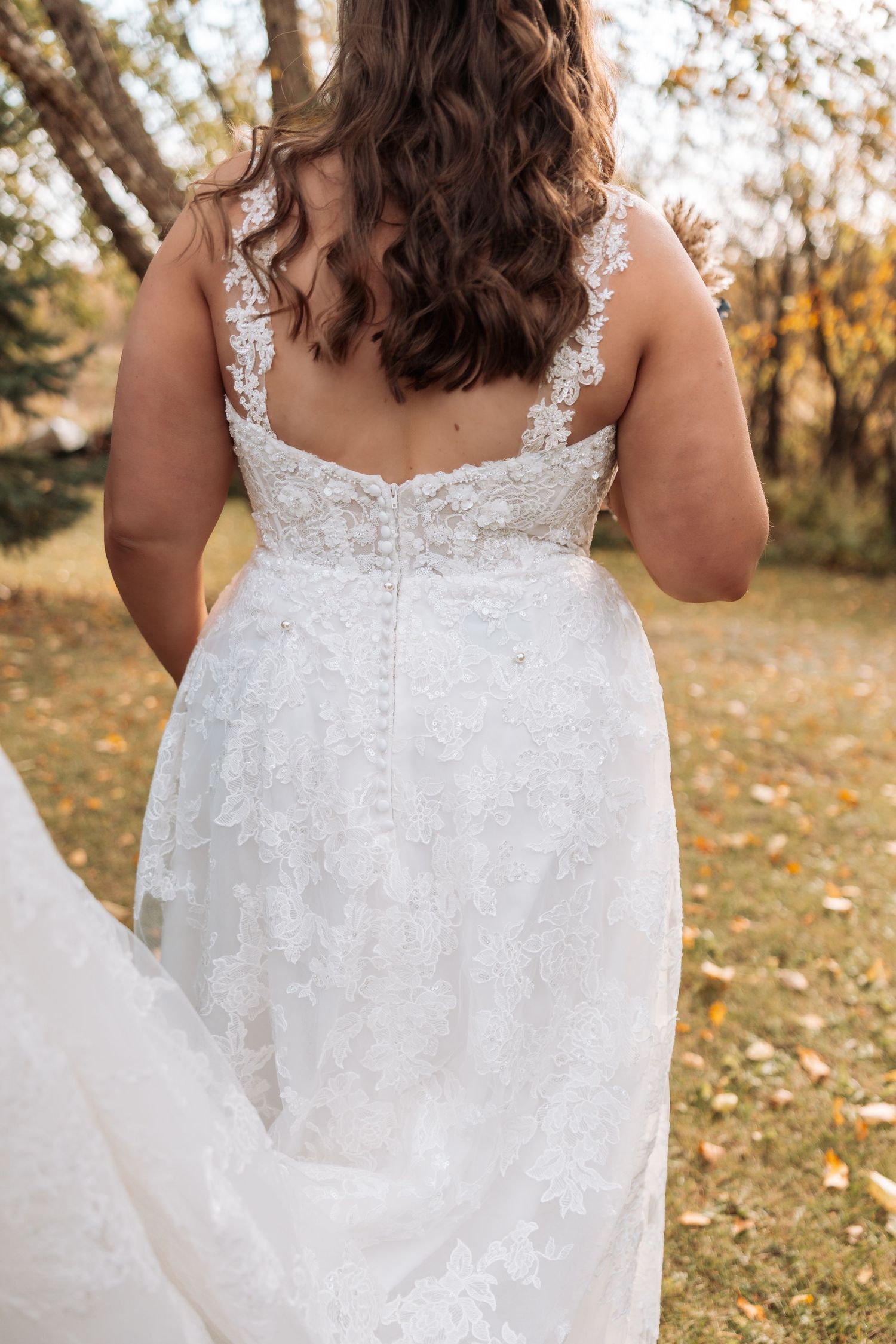 Close-up details of a white lace wedding dress with intricate beading and embroidery against an autumn backdrop.
