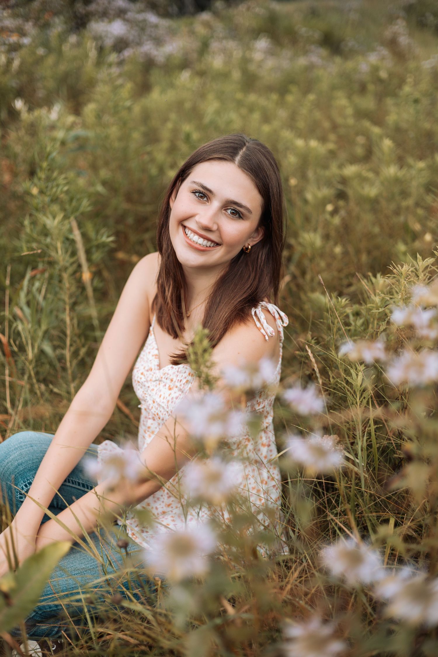 Person sitting in wildflower field wearing white lace top and jeans with Kenzie Ayla Images in the Twin Cities MN area.