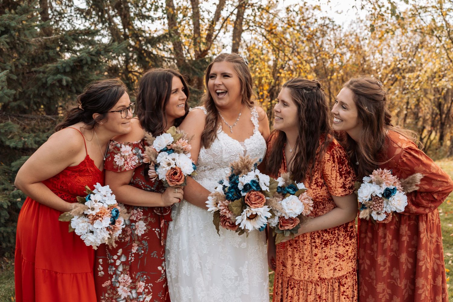 Bridal party in autumn-colored dresses laughing together while holding bouquets.