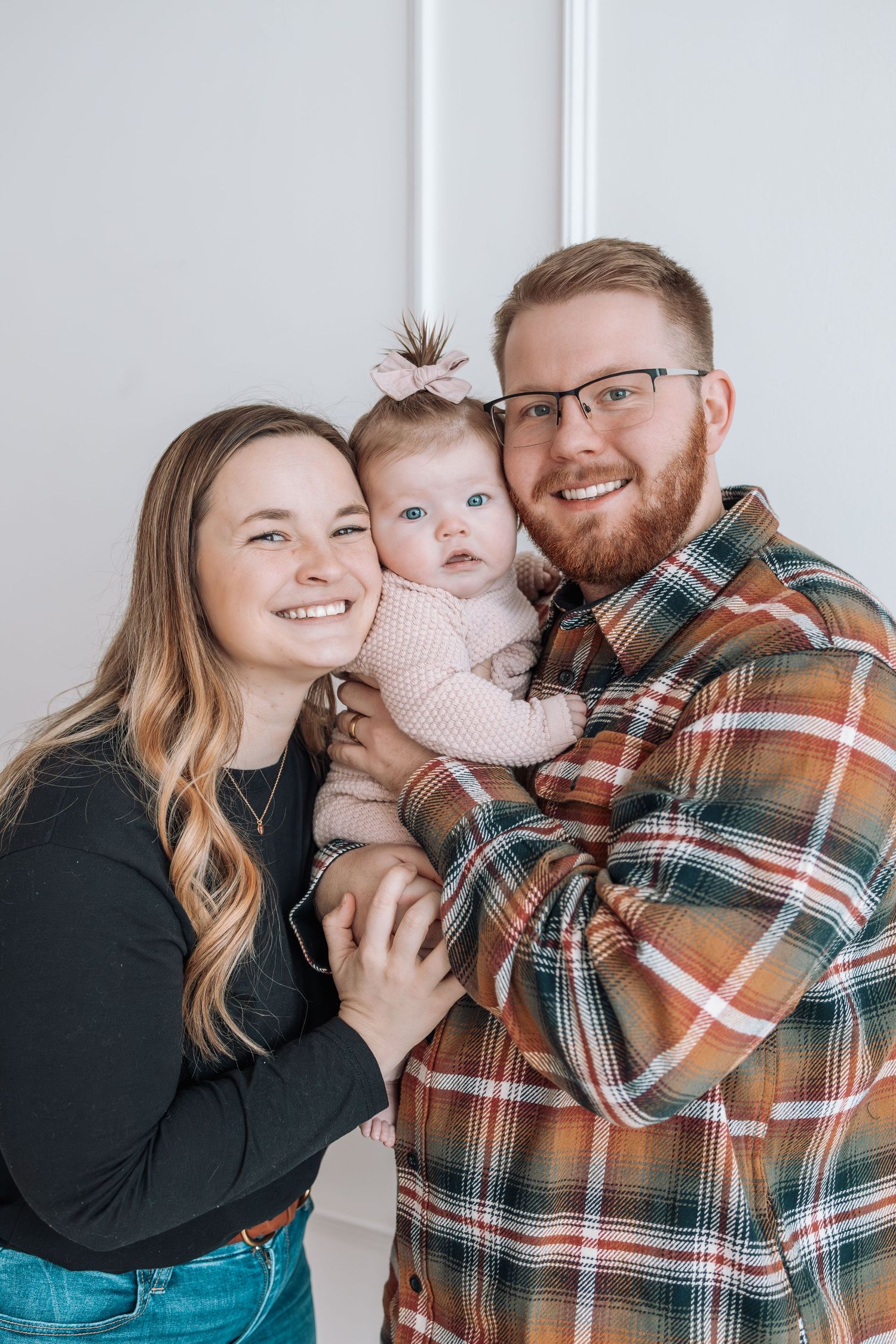 Family shares tender moments and laughter during indoor portrait session against white wall.