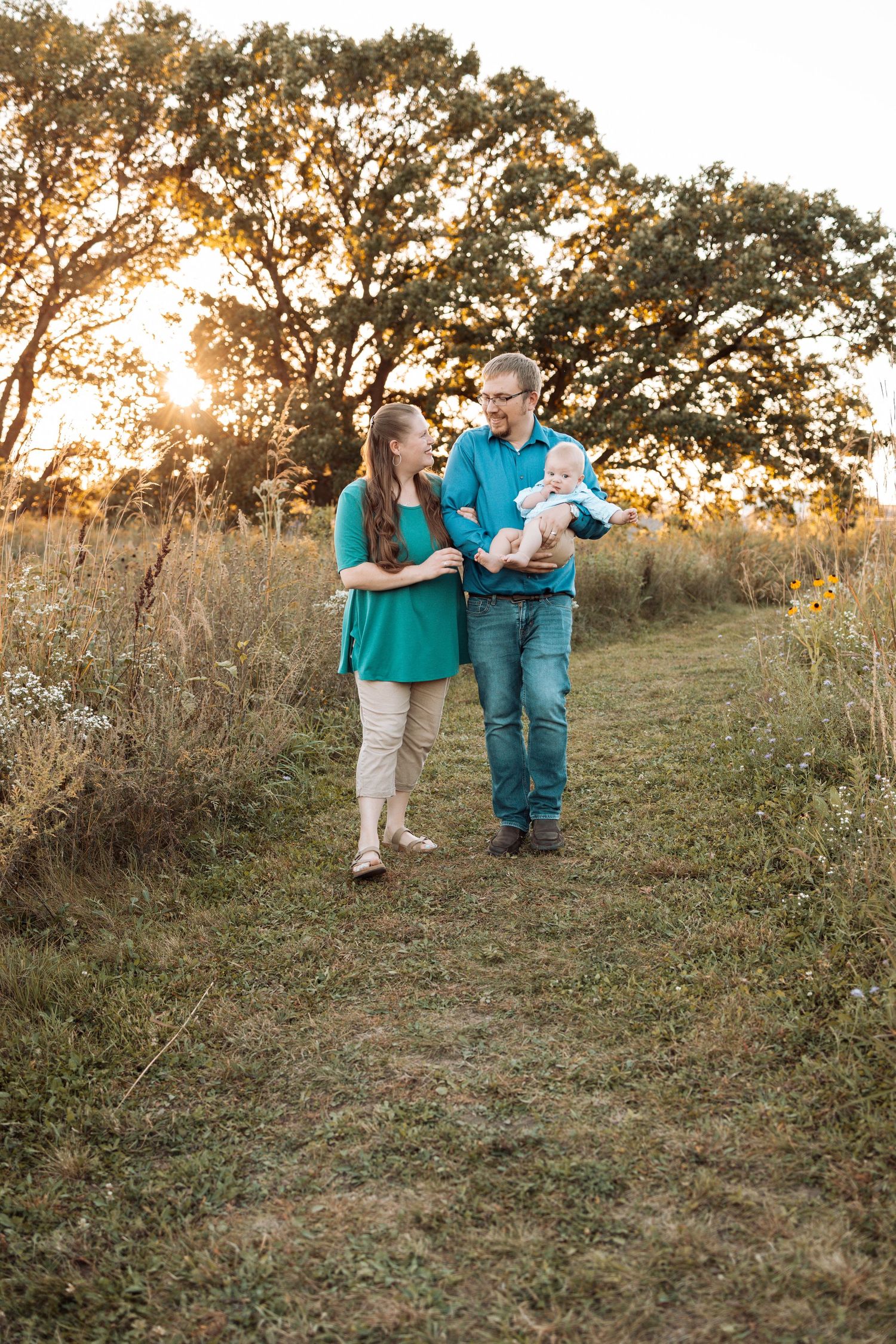 Family playfully interacting on grassy hillside during golden hour.