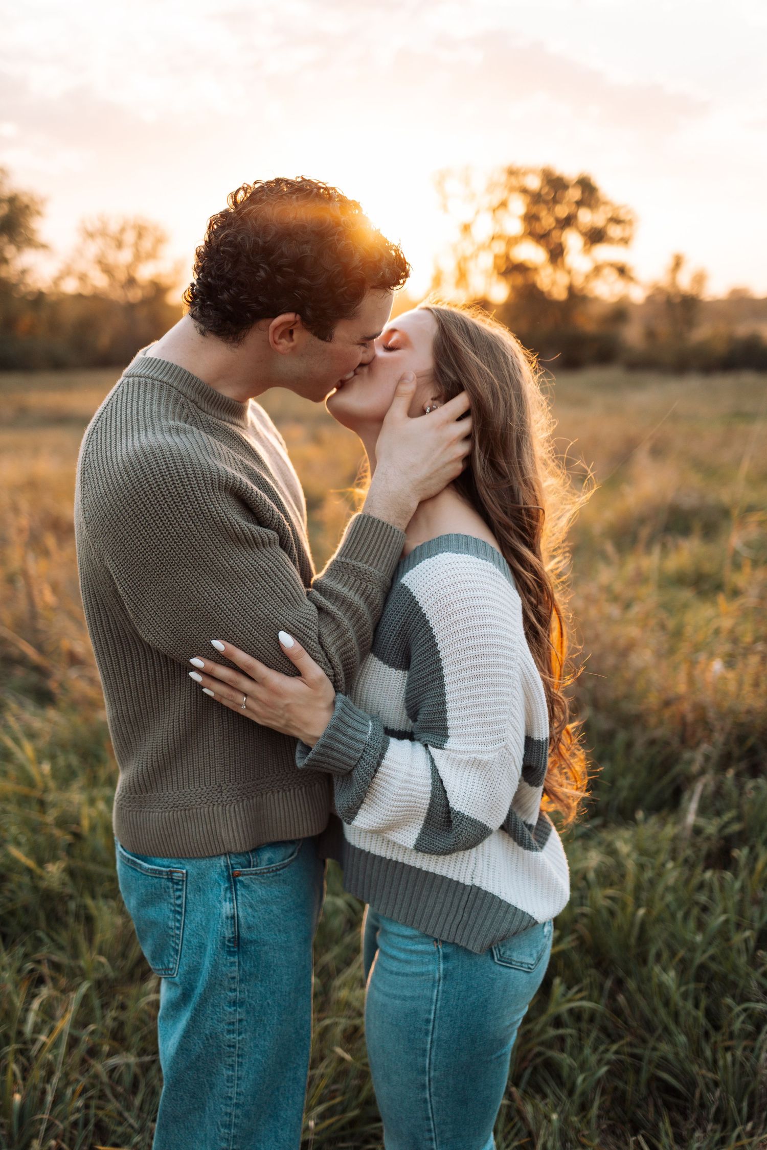 Tender moment between couple in casual wear during sunset in tall grass.
