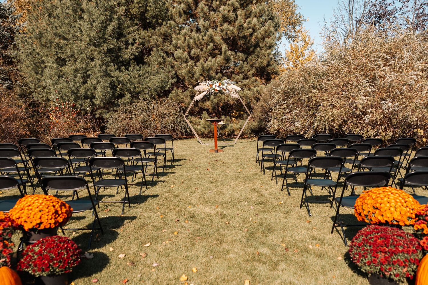 Outdoor wedding ceremony setup with black chairs and orange and red floral arrangements lining the aisle.