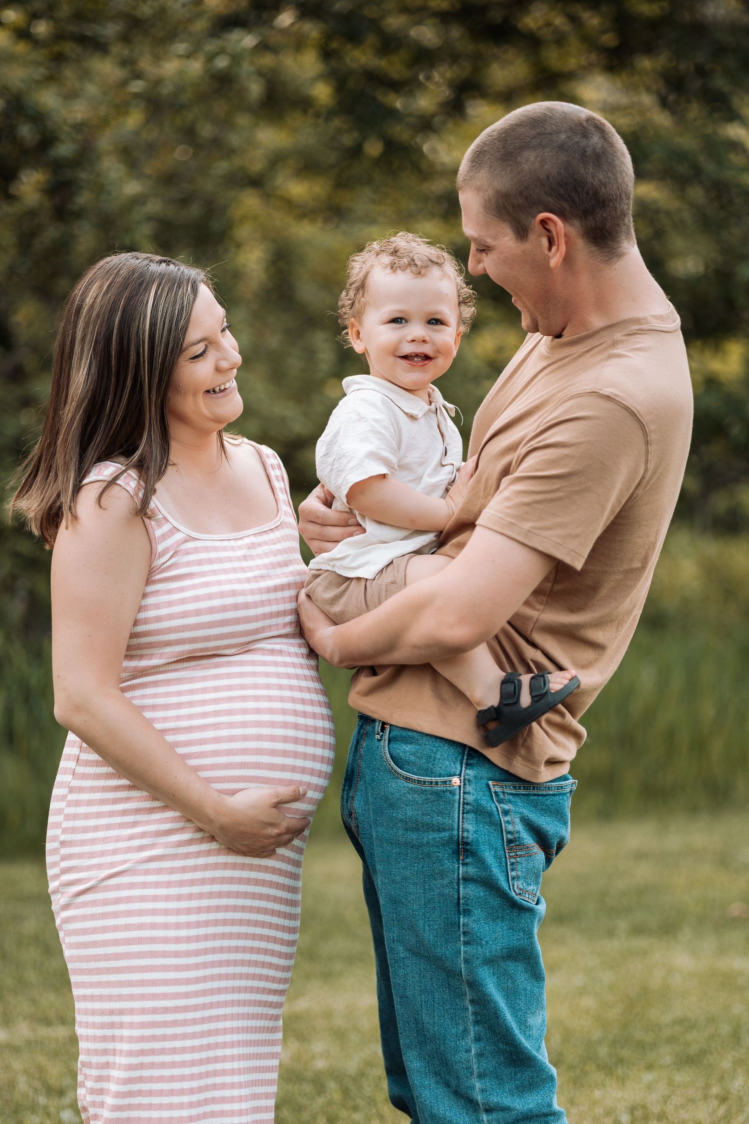Family portrait in a grassy field wearing casual clothes in neutral tones.