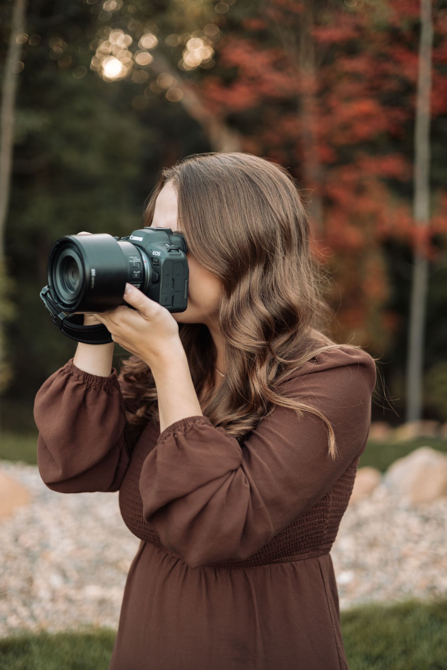Photographer in brown sweater takes photos outdoors during golden hour.