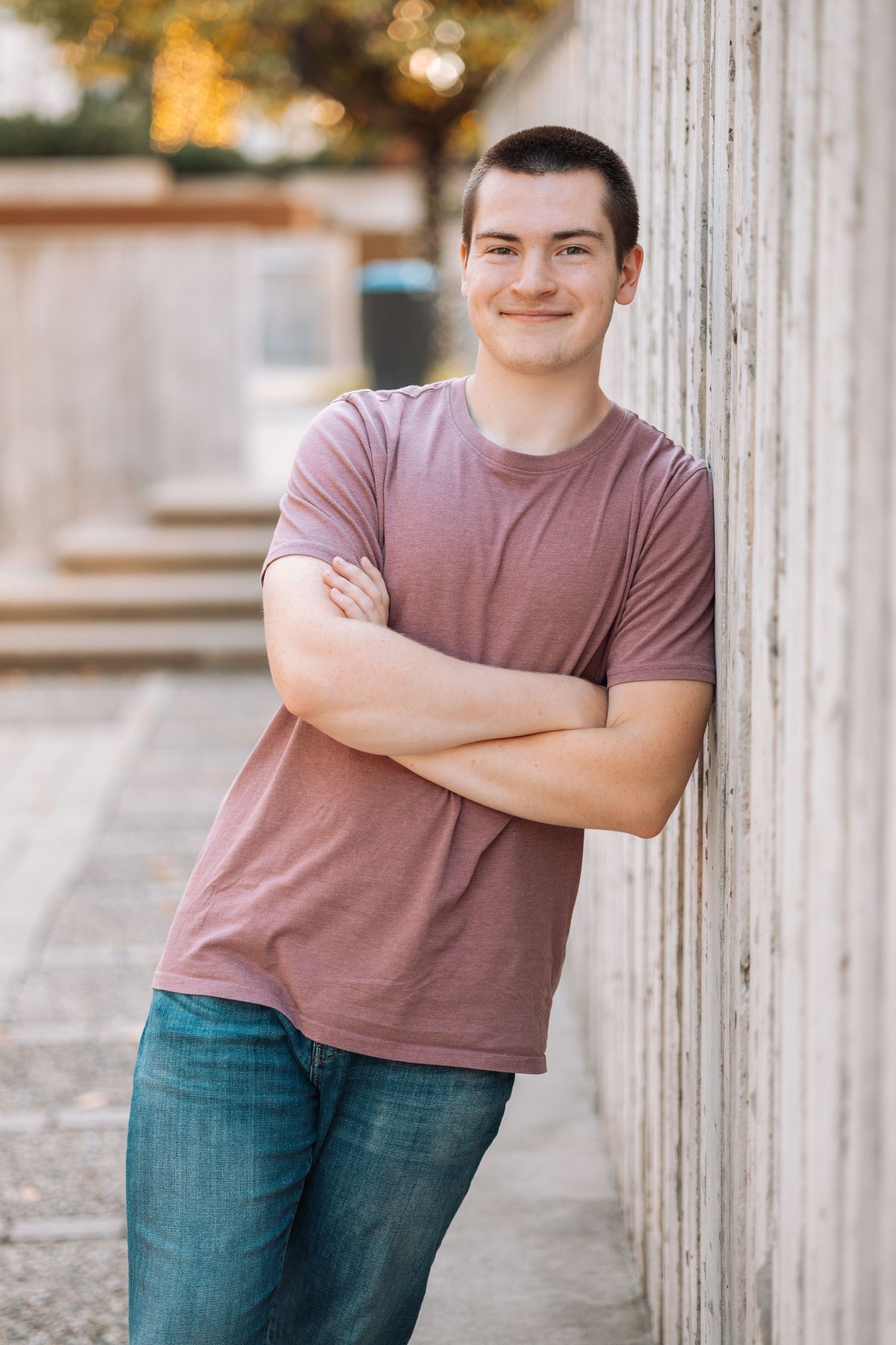 Relaxed outdoor portraits in a mauve t-shirt and jeans leaning against white columns.
