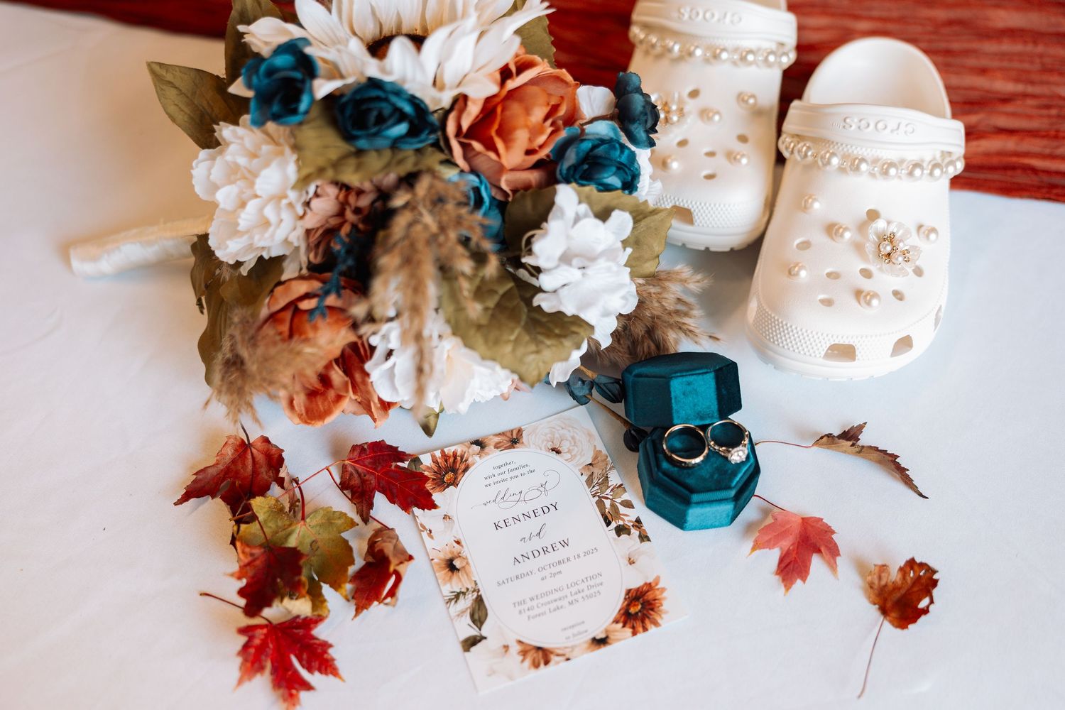 Wedding details flatlay with blue and orange flowers, autumn leaves, and decorative elements.