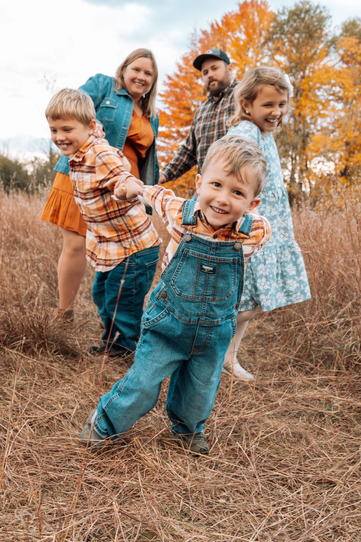 A playful autumn photoshoot in a field with golden foliage and tall grass.