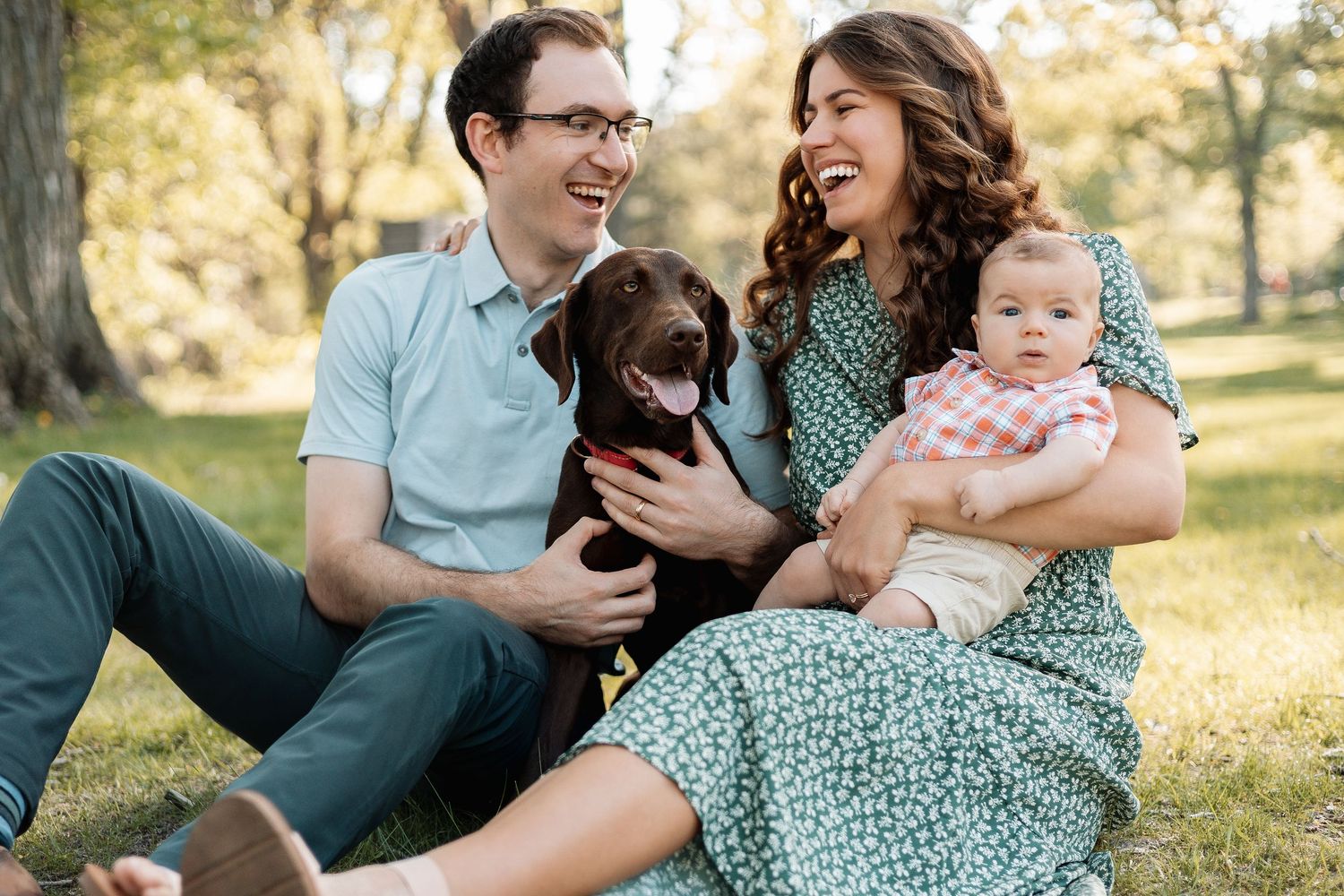 Family relaxing on grass with their dog during a sunny outdoor photo session.