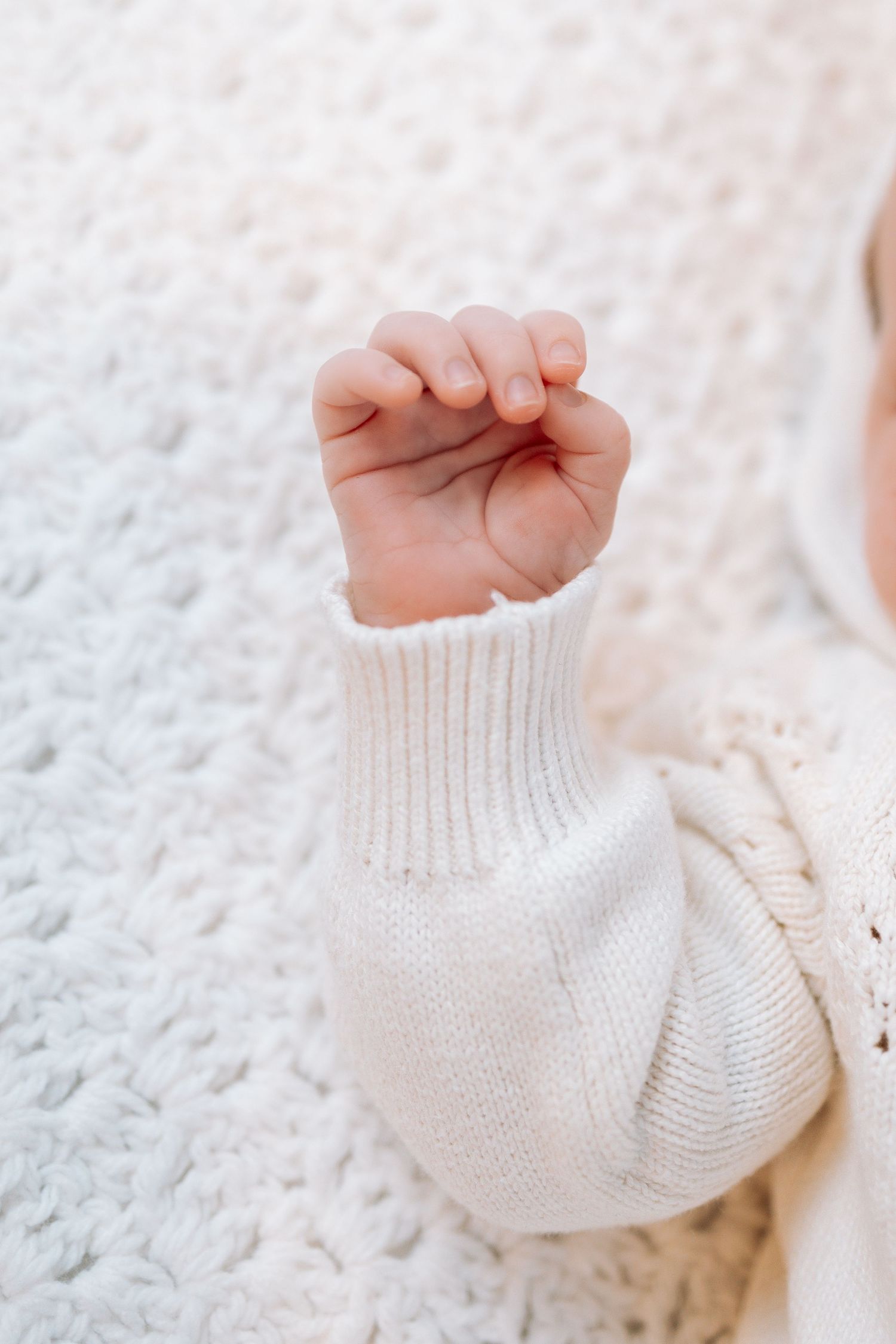 Close-up detail of tiny white knitted baby socks against soft white background.
