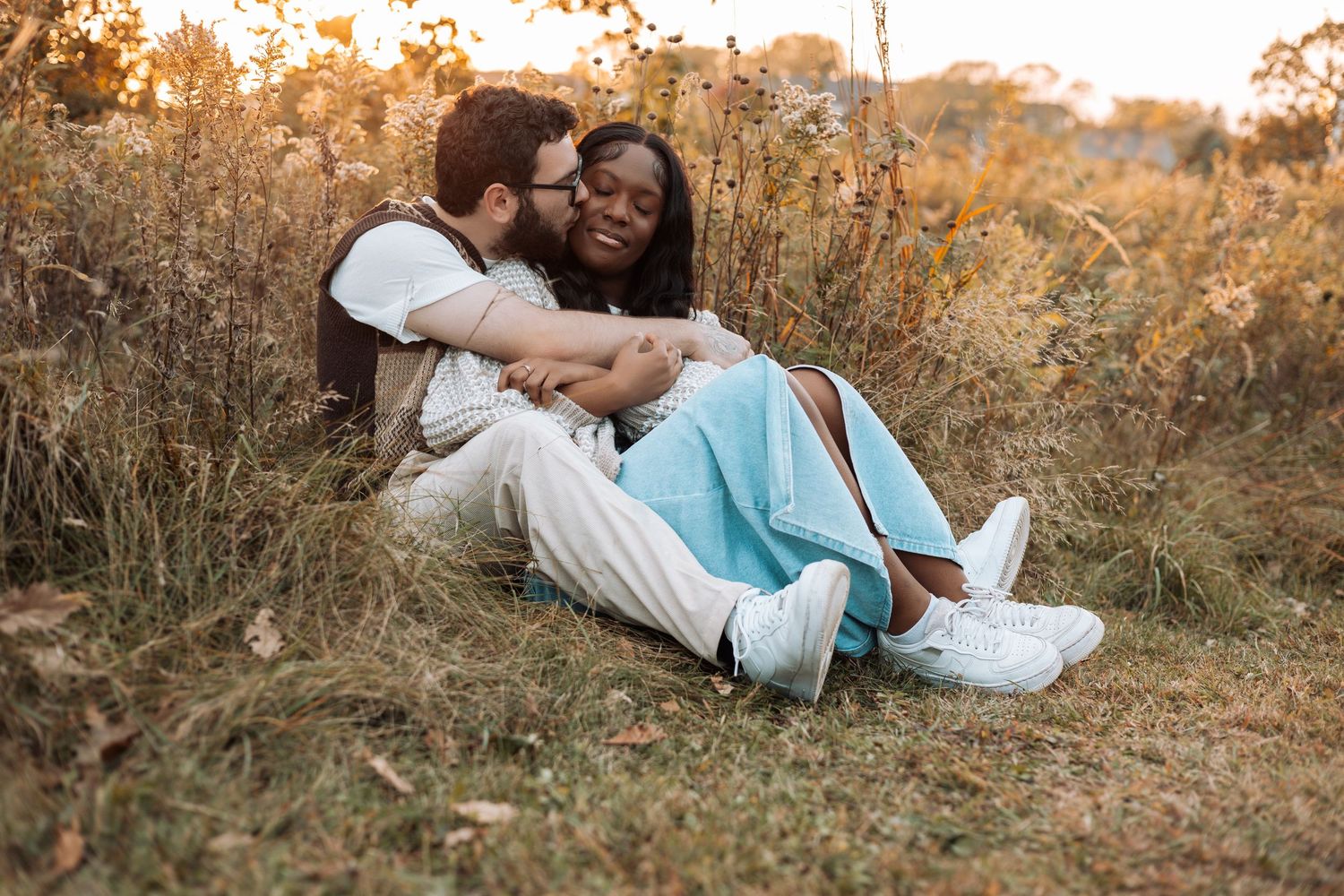A couple embracing on grass during sunset in a romantic outdoor photoshoot.