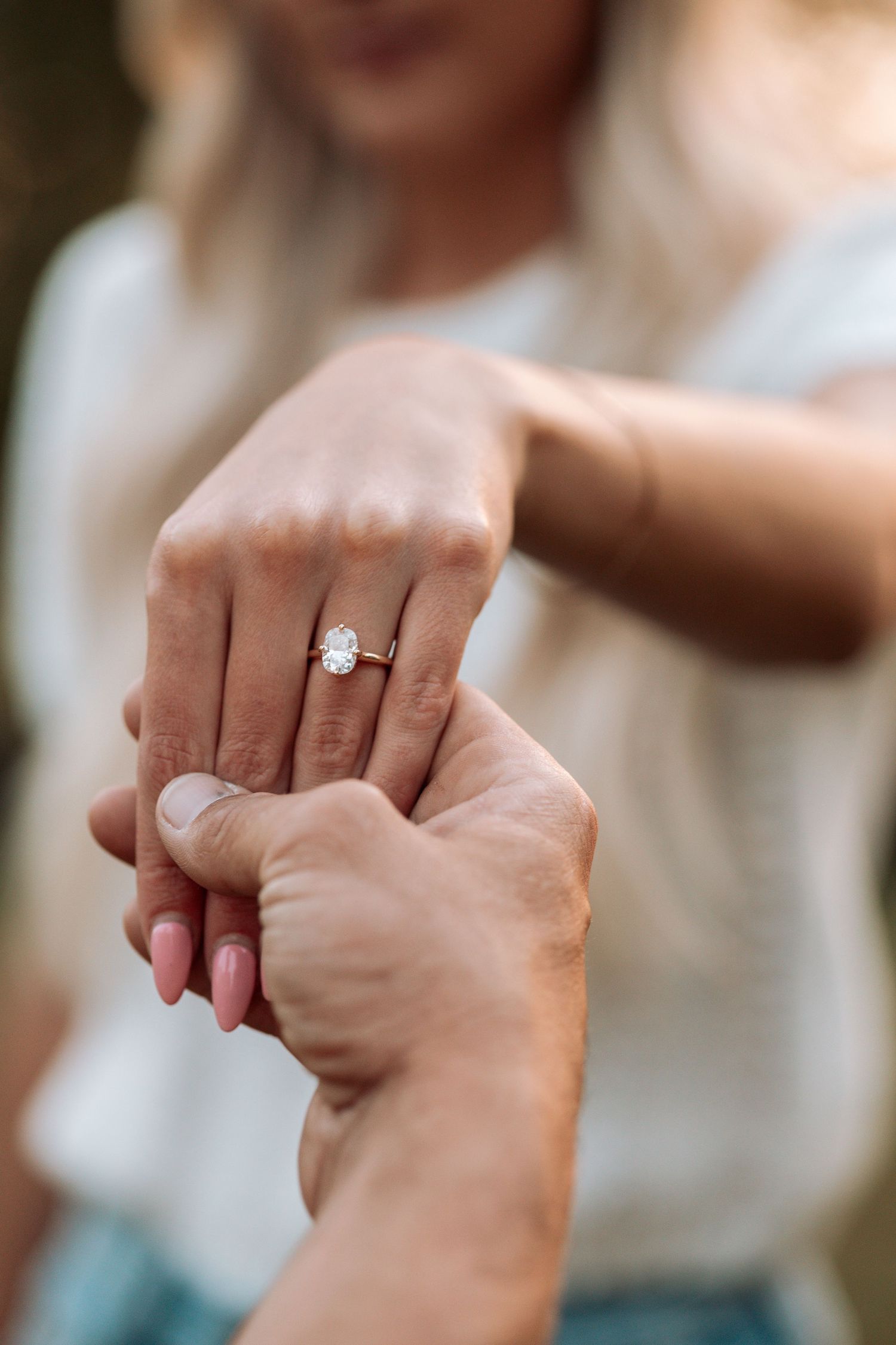 Close-up shot of hands displaying an engagement ring in natural lighting.