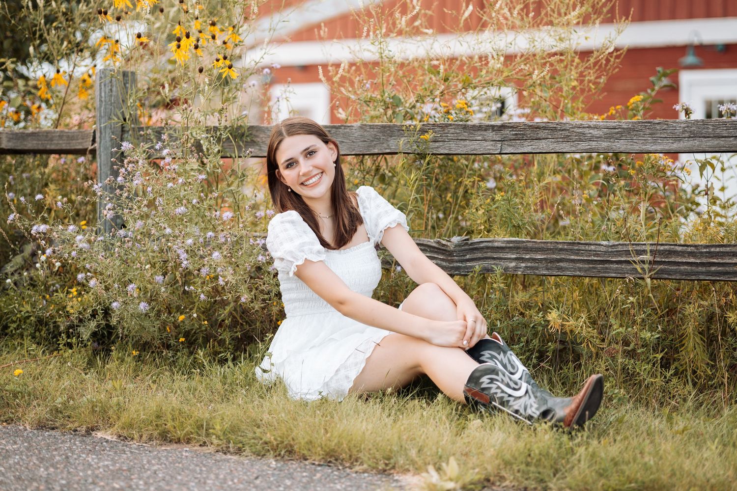 Person in white dress and boots sits by rustic fence in autumn setting with Kenzie Ayla Images in the Twin Cities MN area.
