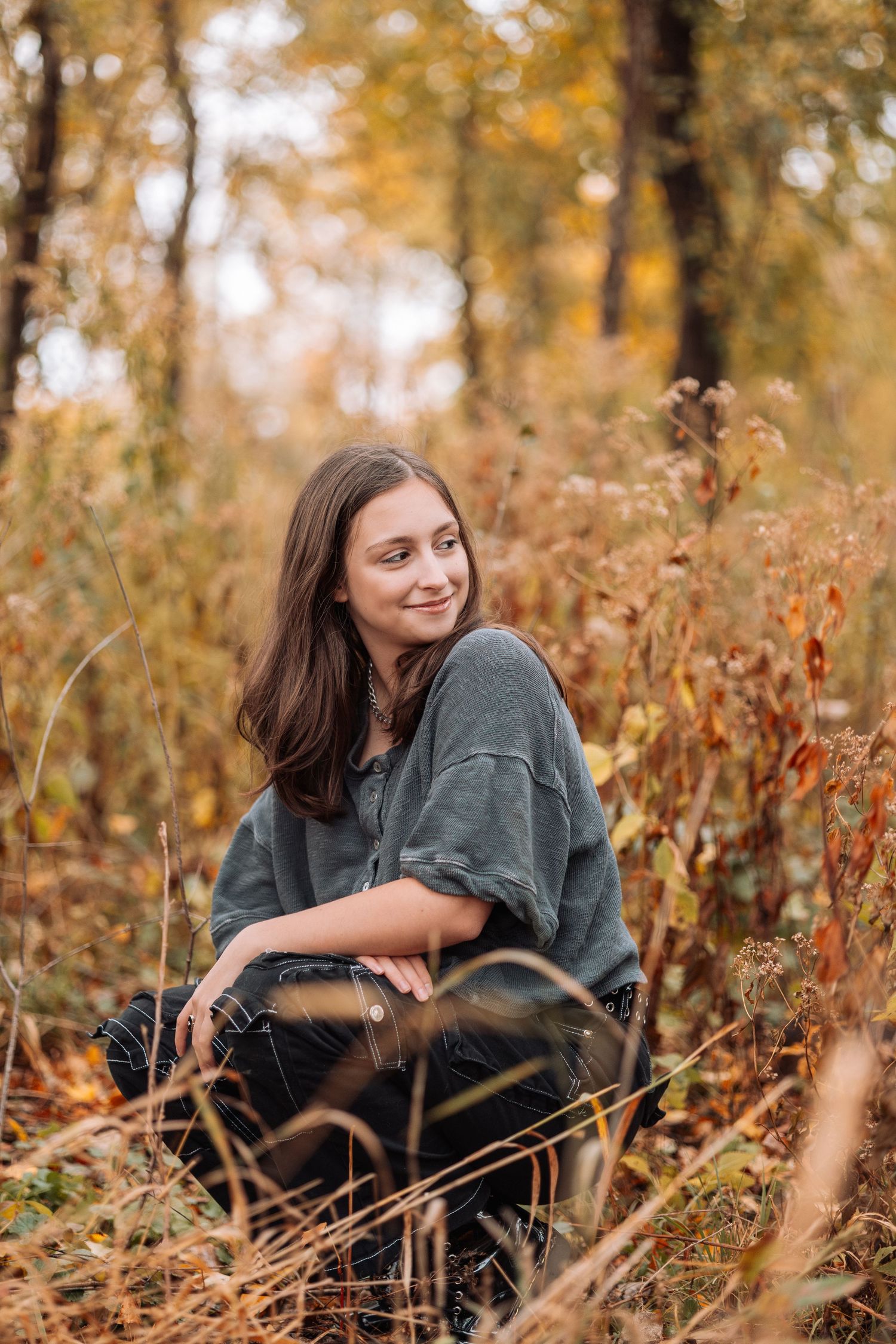 Person in grey sweater lying in autumn foliage during outdoor photoshoot.