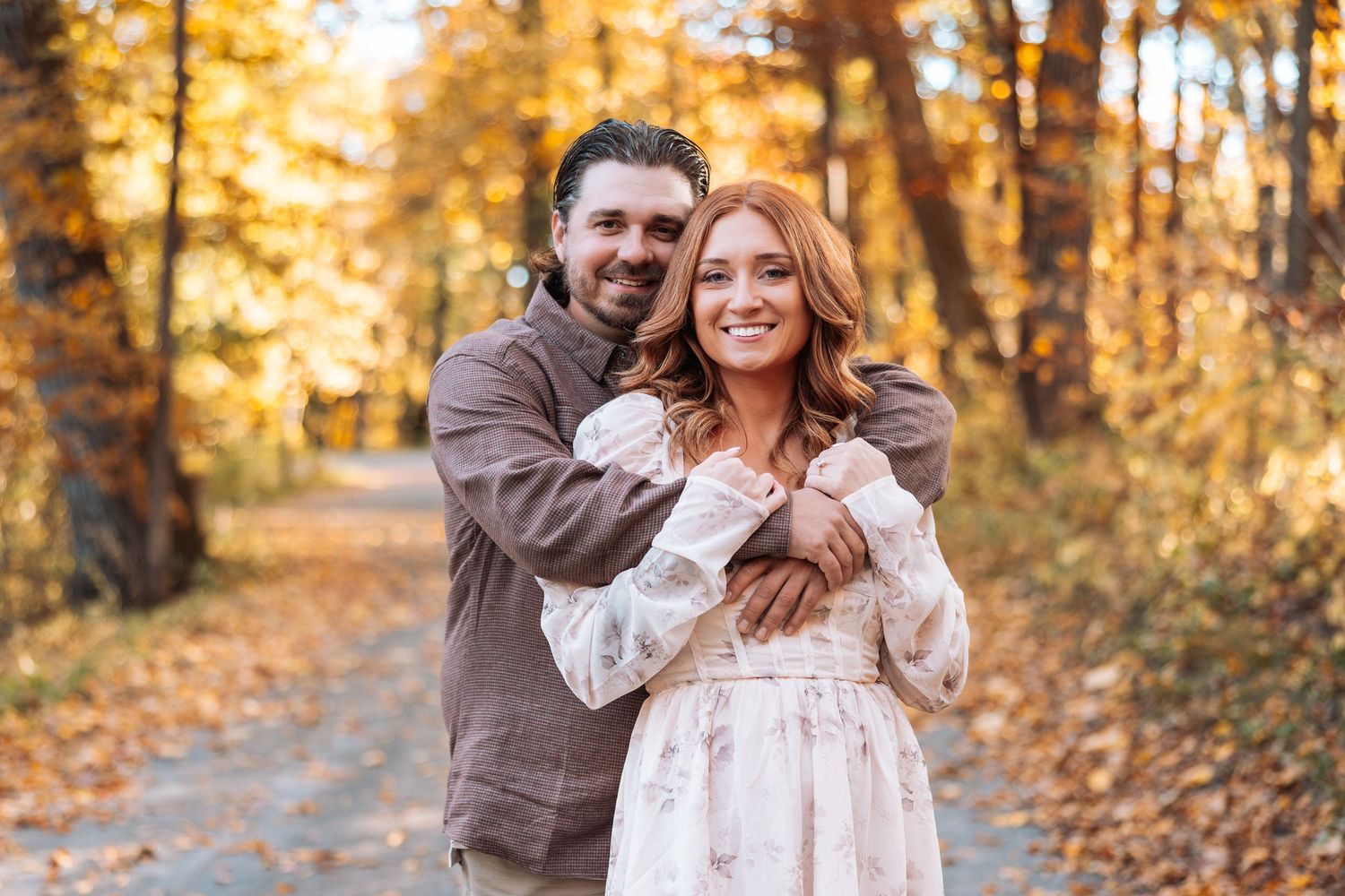Couple embracing in a golden autumn forest with sunlight filtering through the trees.