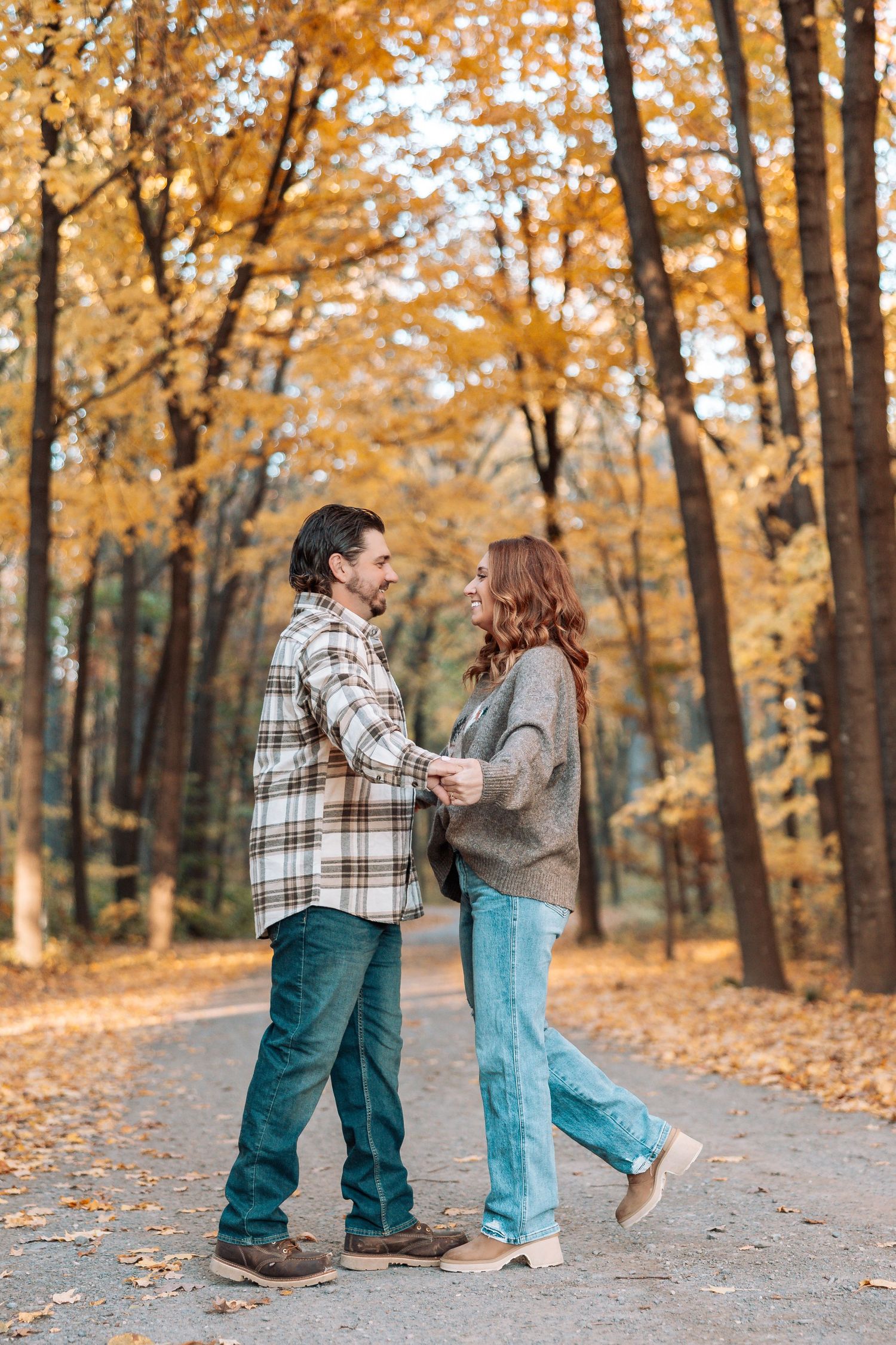 Playful couple dancing together on a leaf-covered path in autumn woods.