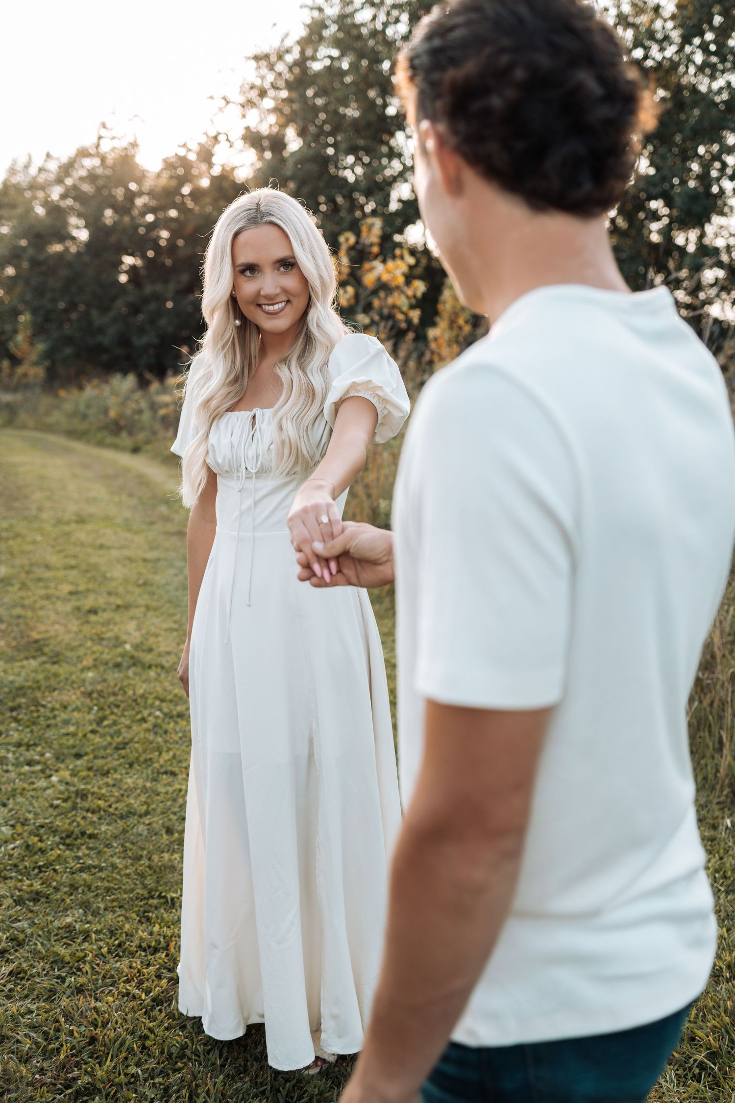 A couple in coordinated white outfits sharing playful moments outdoors.