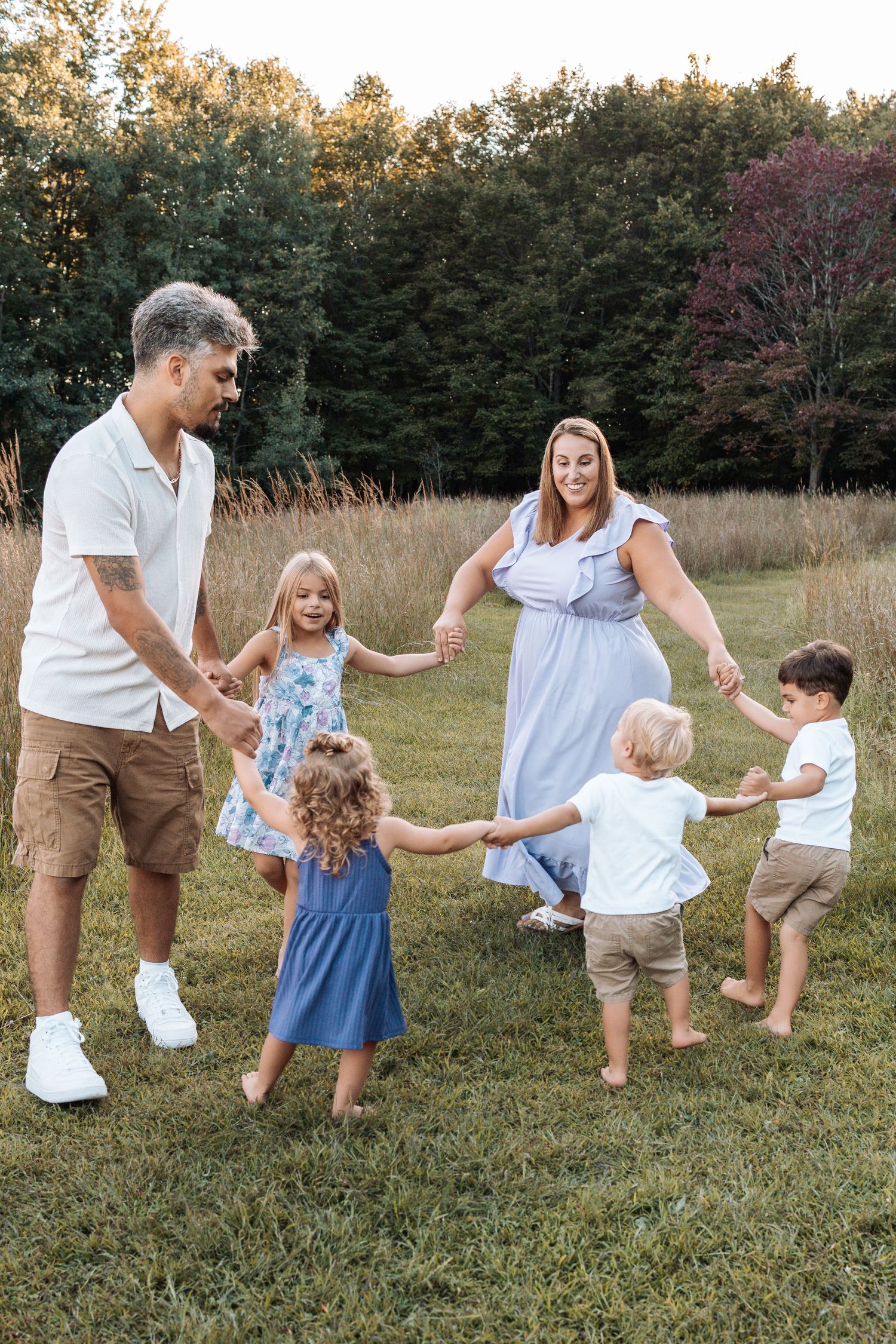 Family plays together in a grassy field during golden hour, holding hands and dancing in a line.