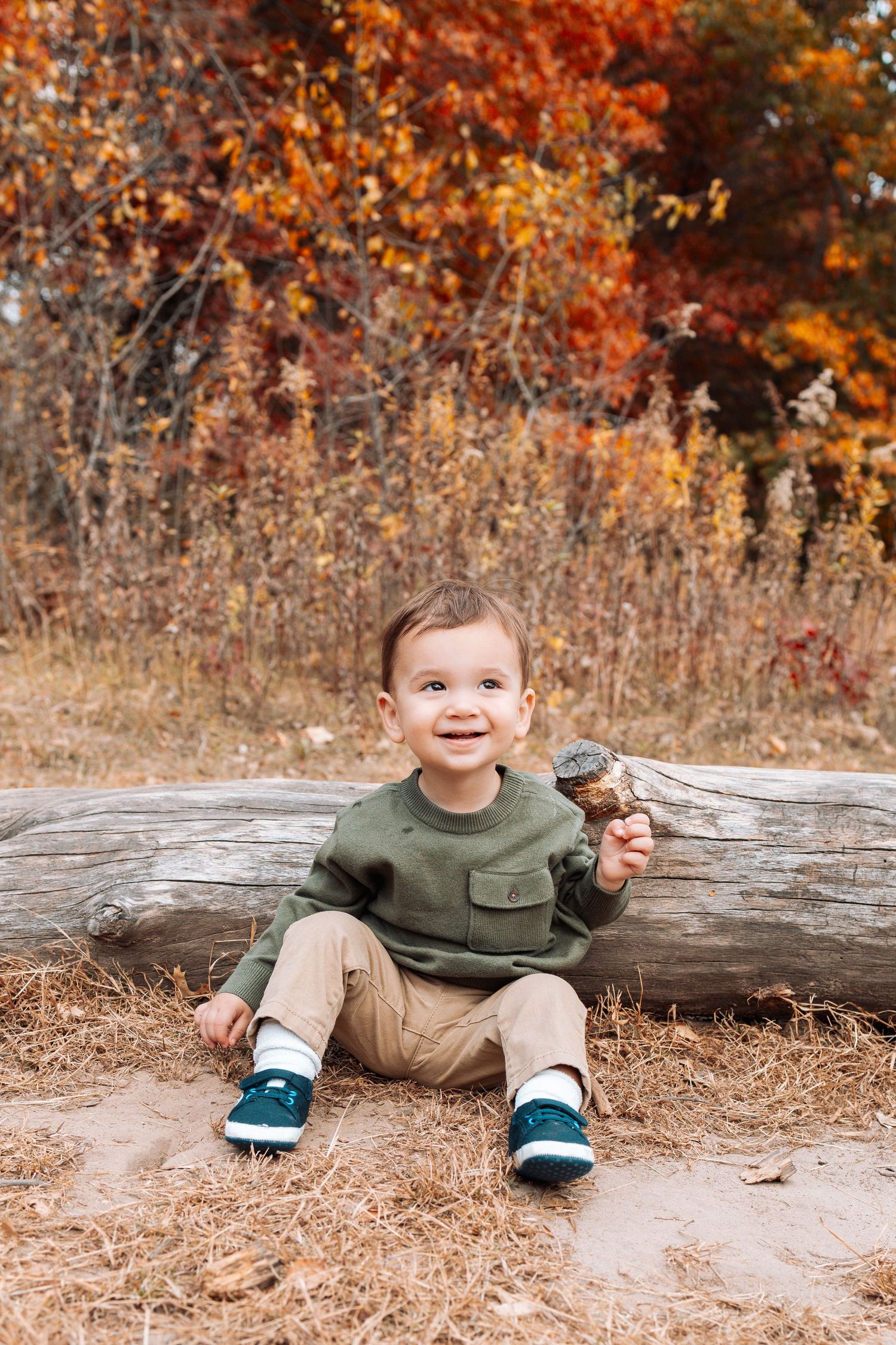 Child sitting on fallen log during autumn photoshoot with orange foliage background.