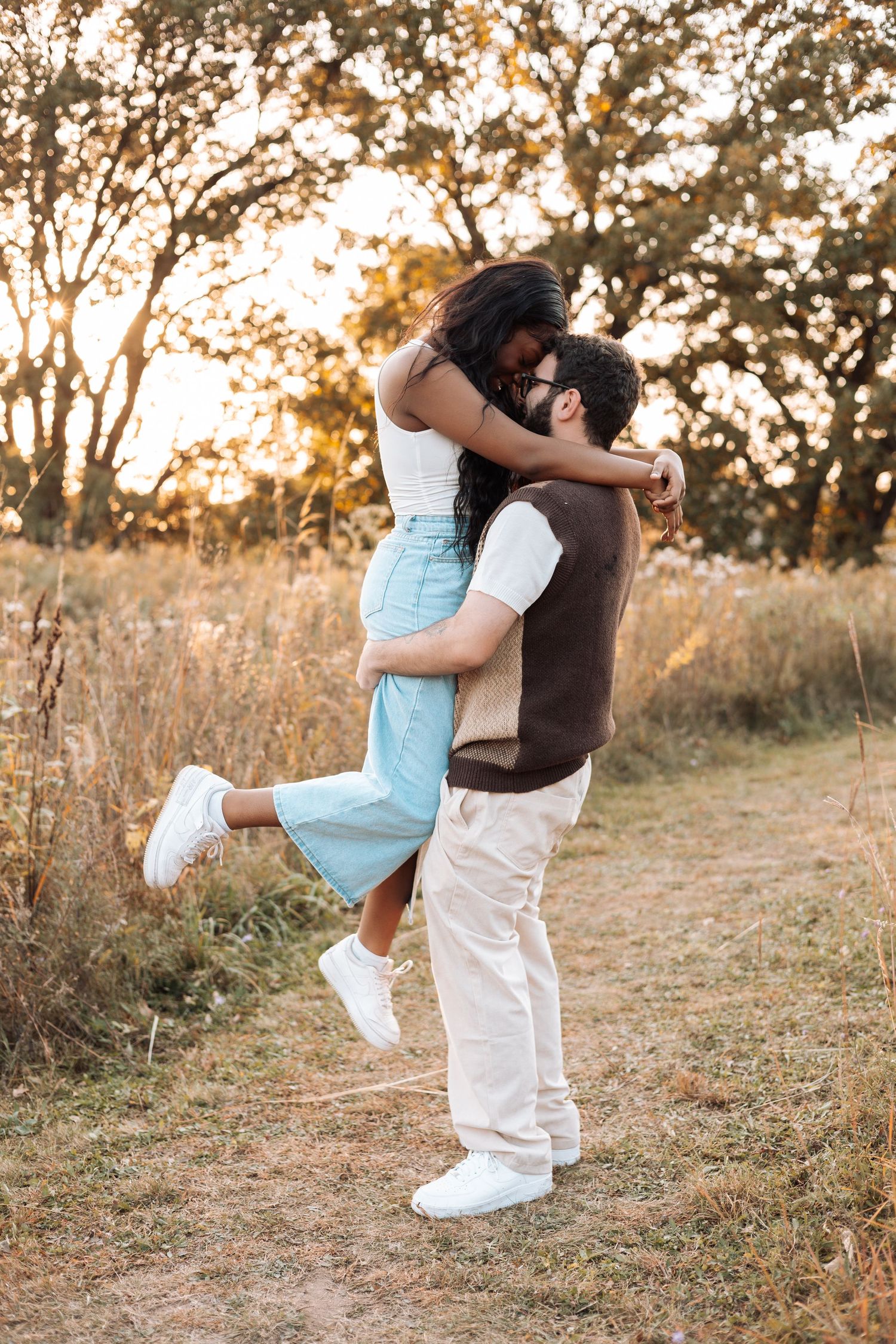 Couple in white outfits sharing playful dance moves in golden sunlight.