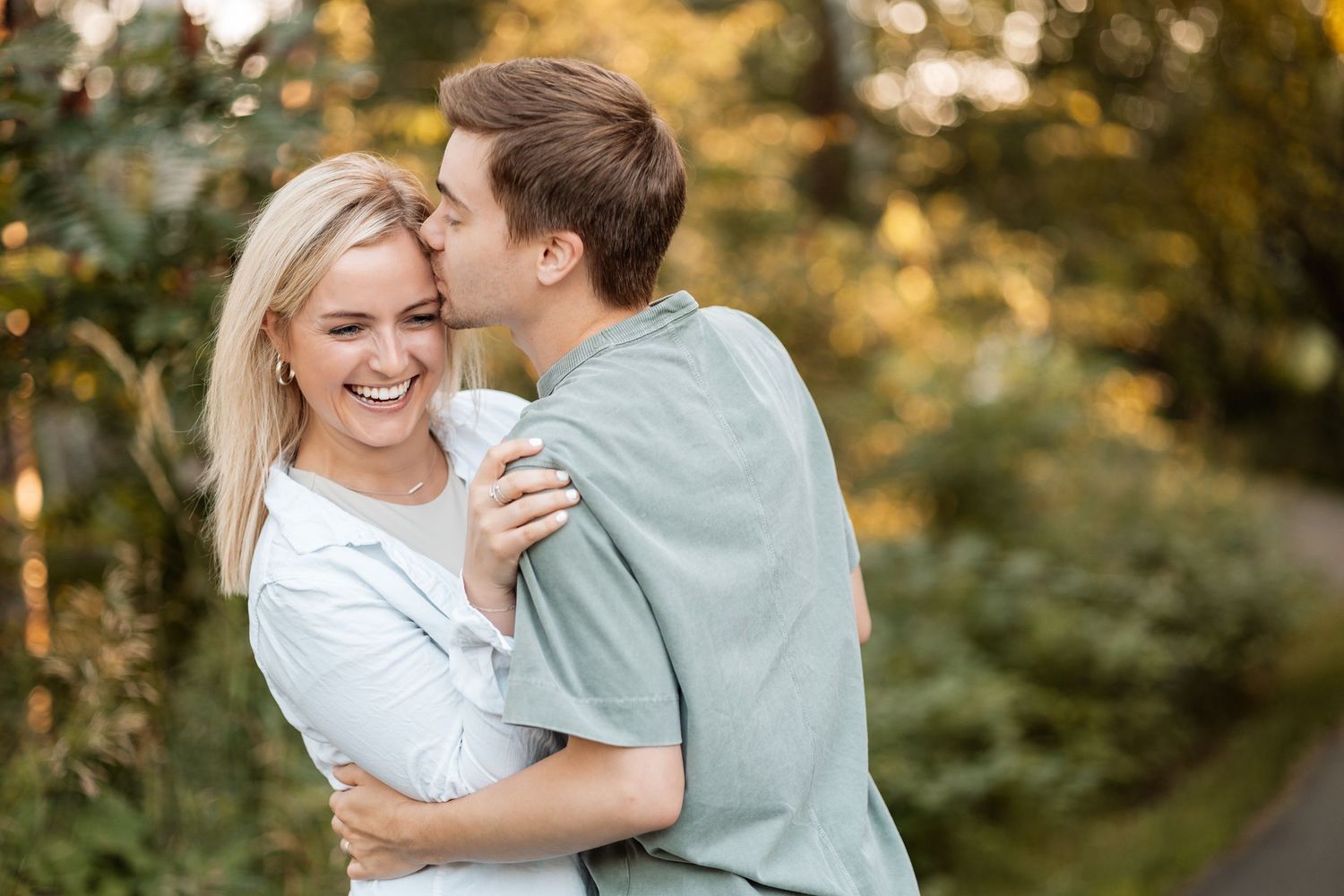 Romantic couple sharing intimate moments in a sunlit outdoor setting with natural greenery.