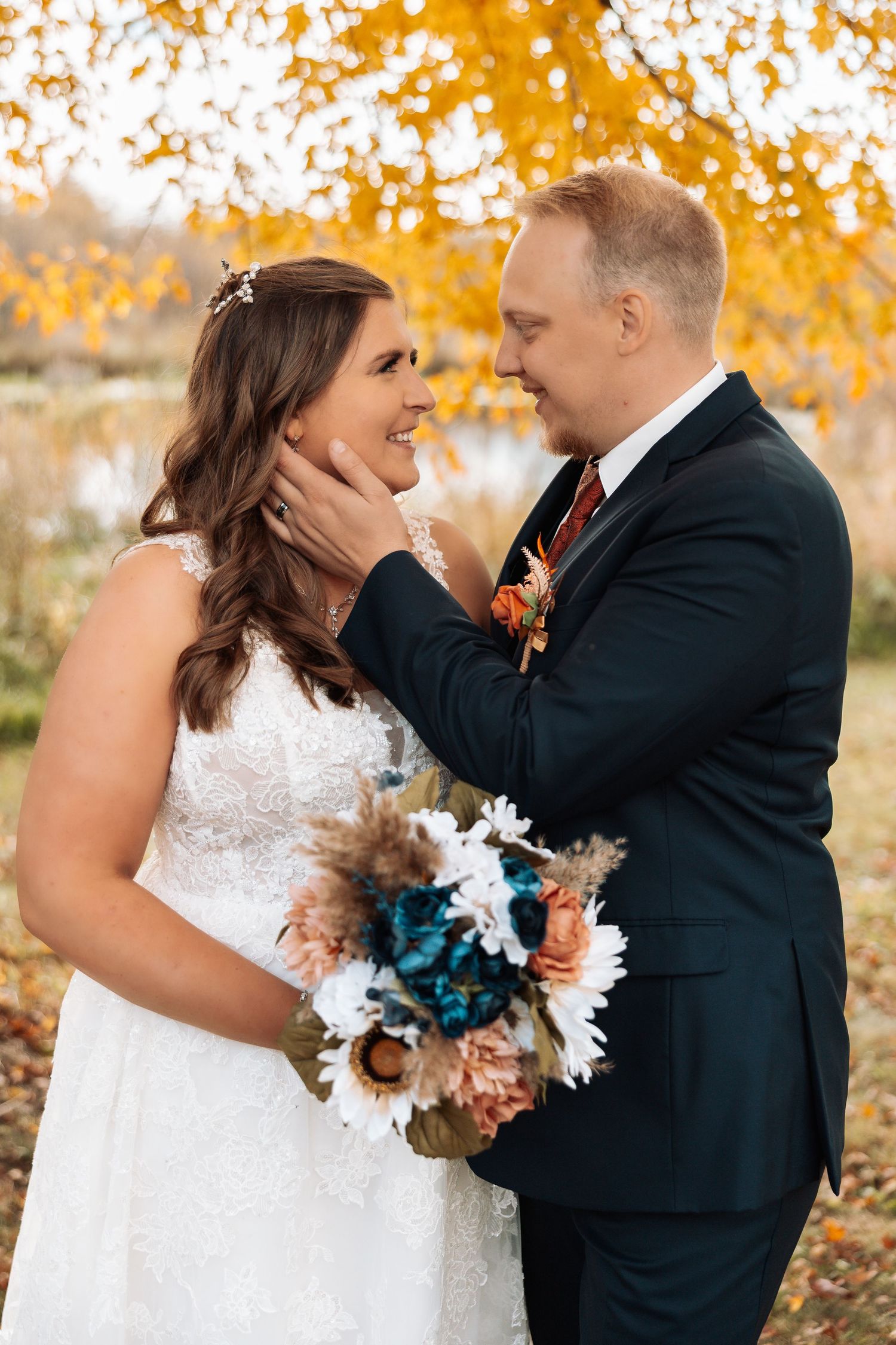 A romantic wedding moment captured outdoors with fall foliage and a blue and white bouquet.