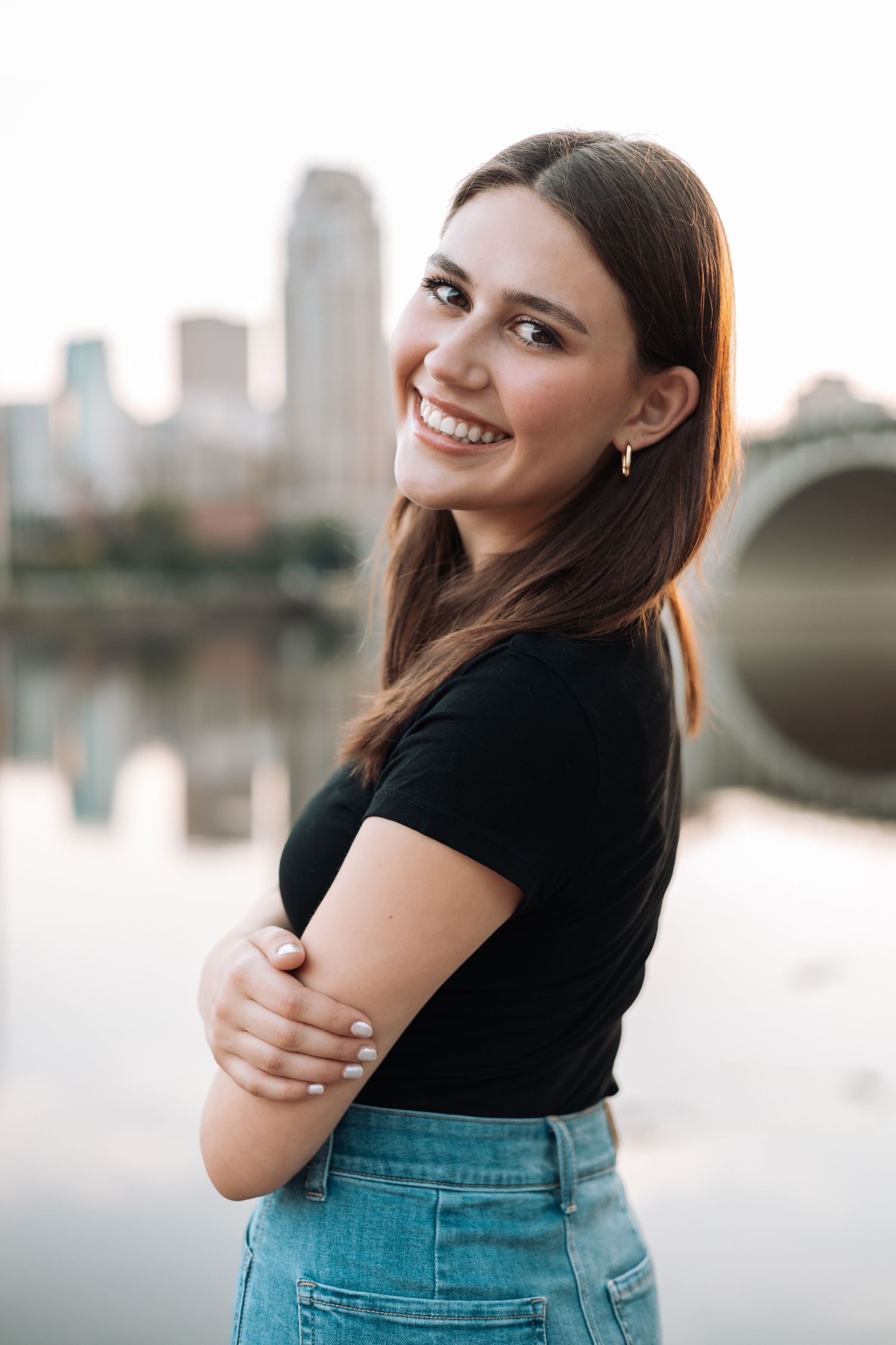 Person in black top and jeans poses against city skyline backdrop with Kenzie Ayla Images in the Twin Cities MN area.