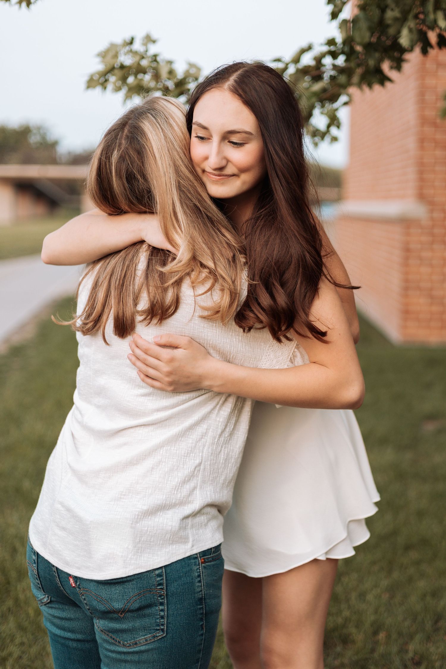 Two people in white tops and jeans sharing a warm embrace outdoors.