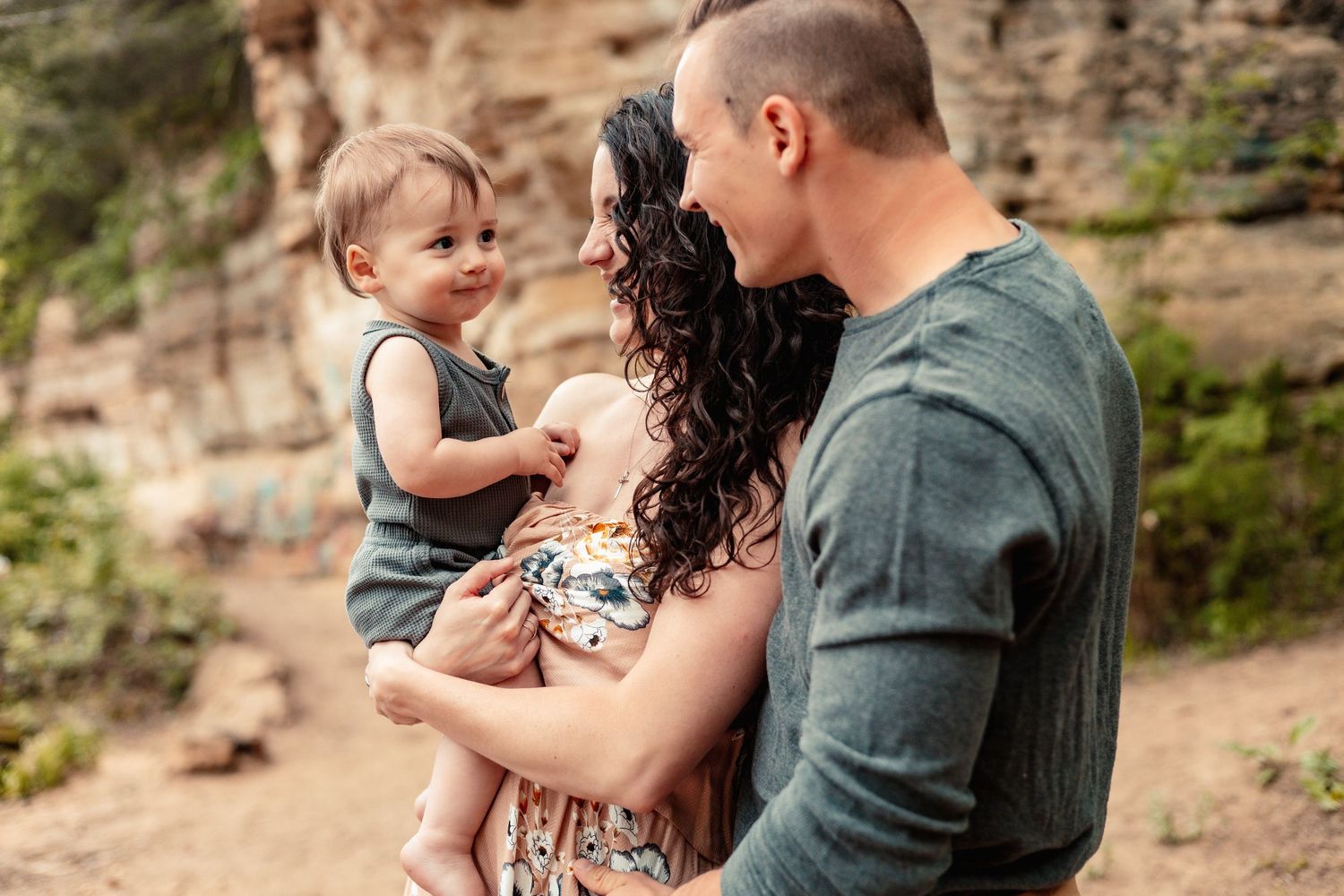 A couple shares tender moments with their baby against a rocky outdoor backdrop.
