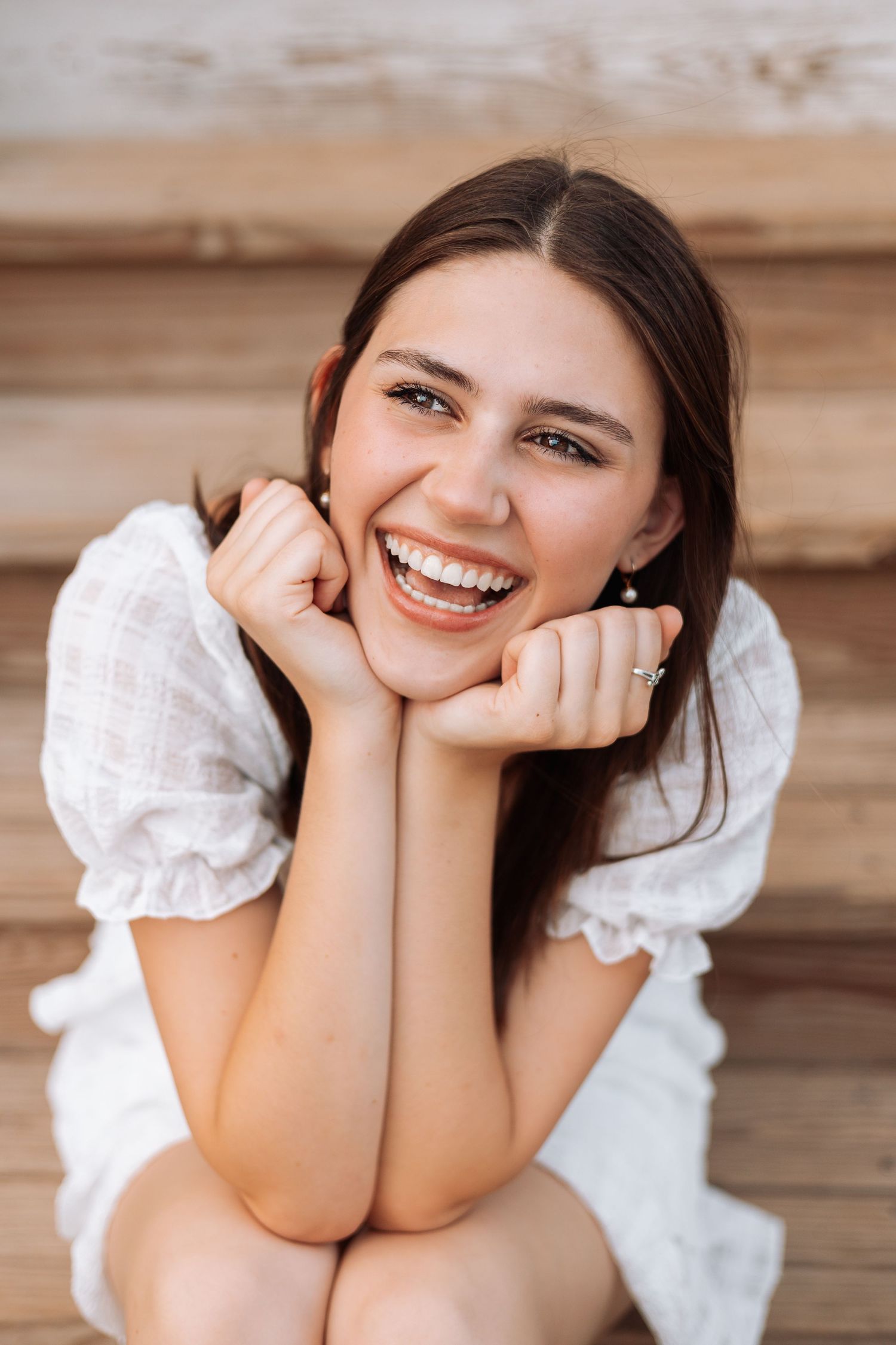 Portrait of person in white ruffled top smiling joyfully against wooden background.
