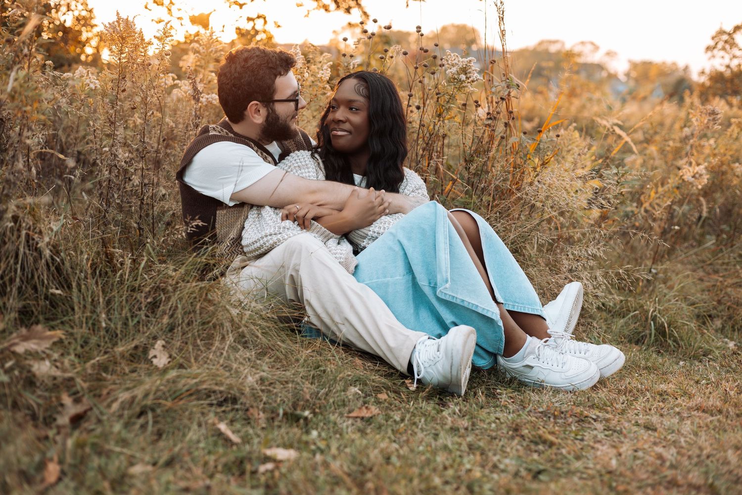 Couple lying in golden grass during autumn sunset photoshoot.