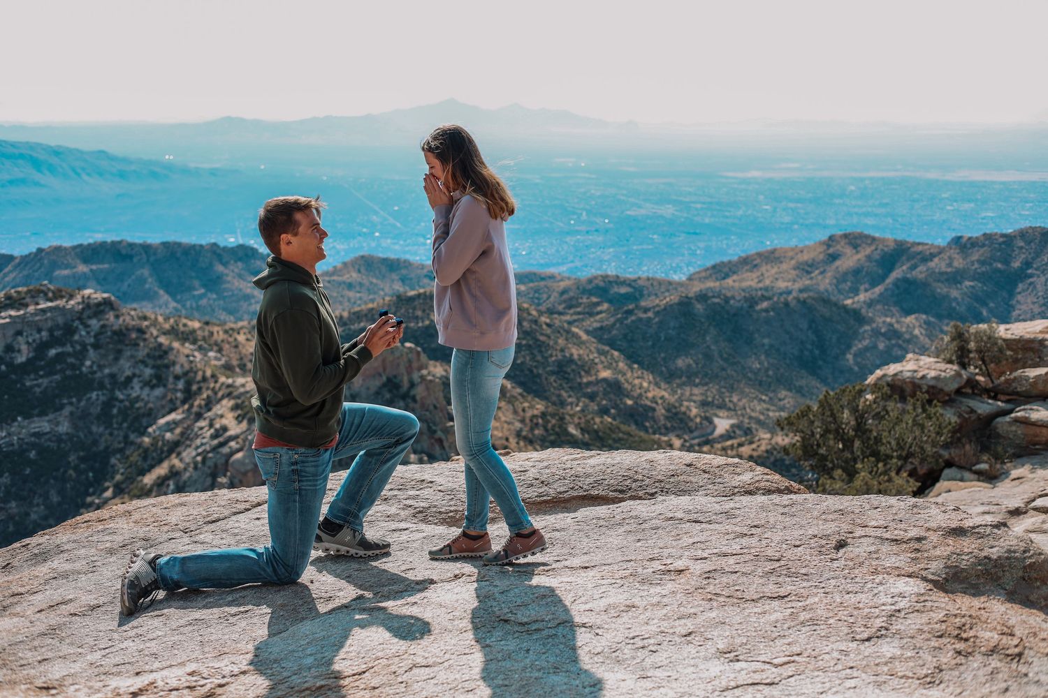 Proposal moment captured on a scenic mountain overlook with vast mountain ranges in the background.