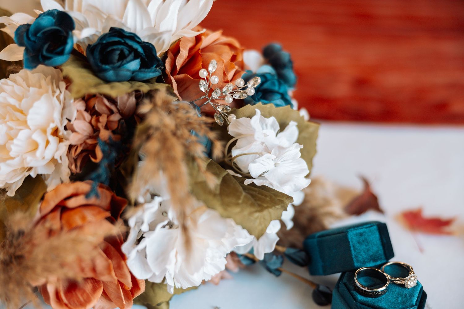 Wedding bouquet with blue and coral flowers alongside wedding rings and teal accents.