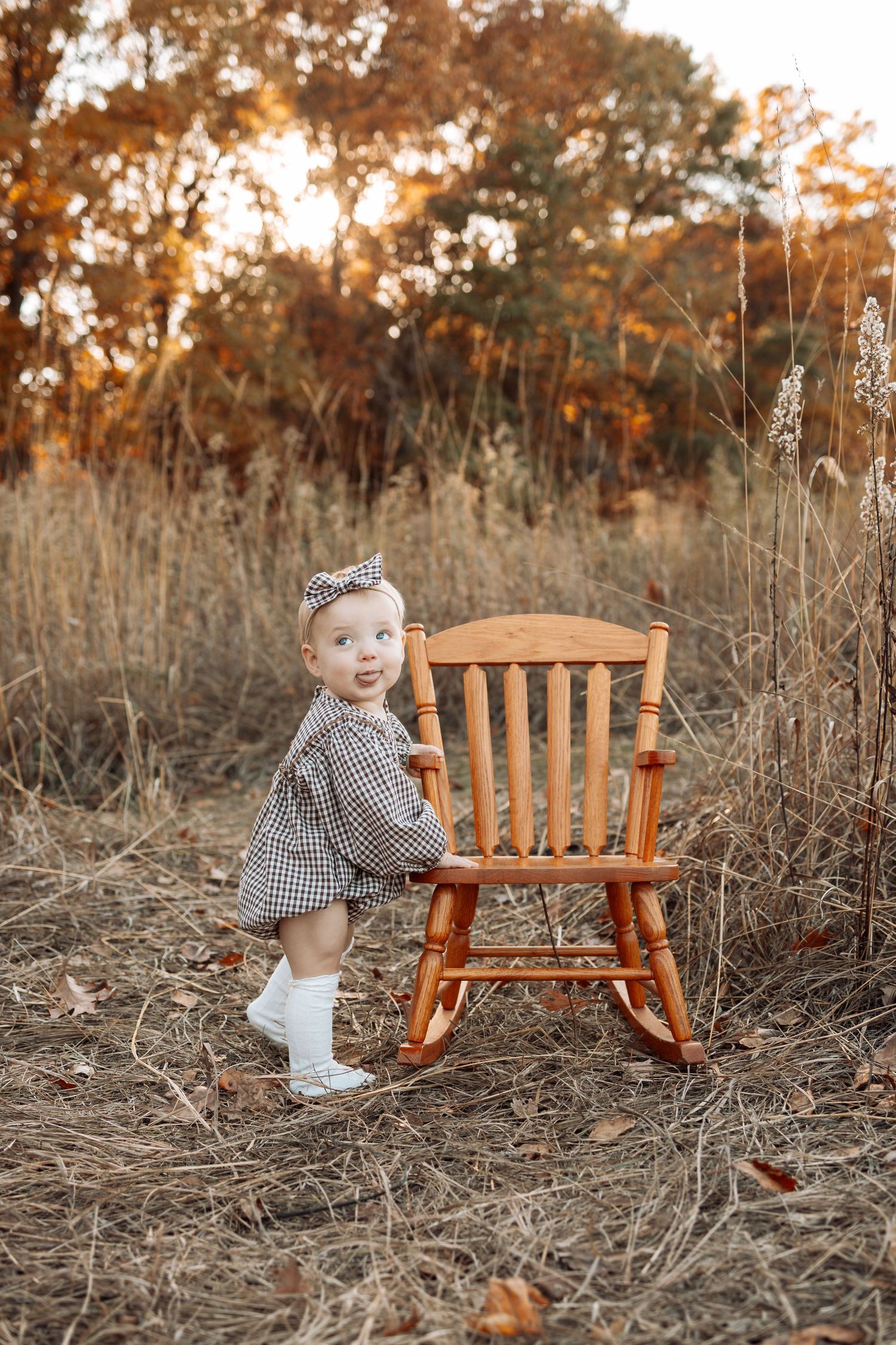 Wooden rocking chair sits in a field of tall grass during golden hour sunset.